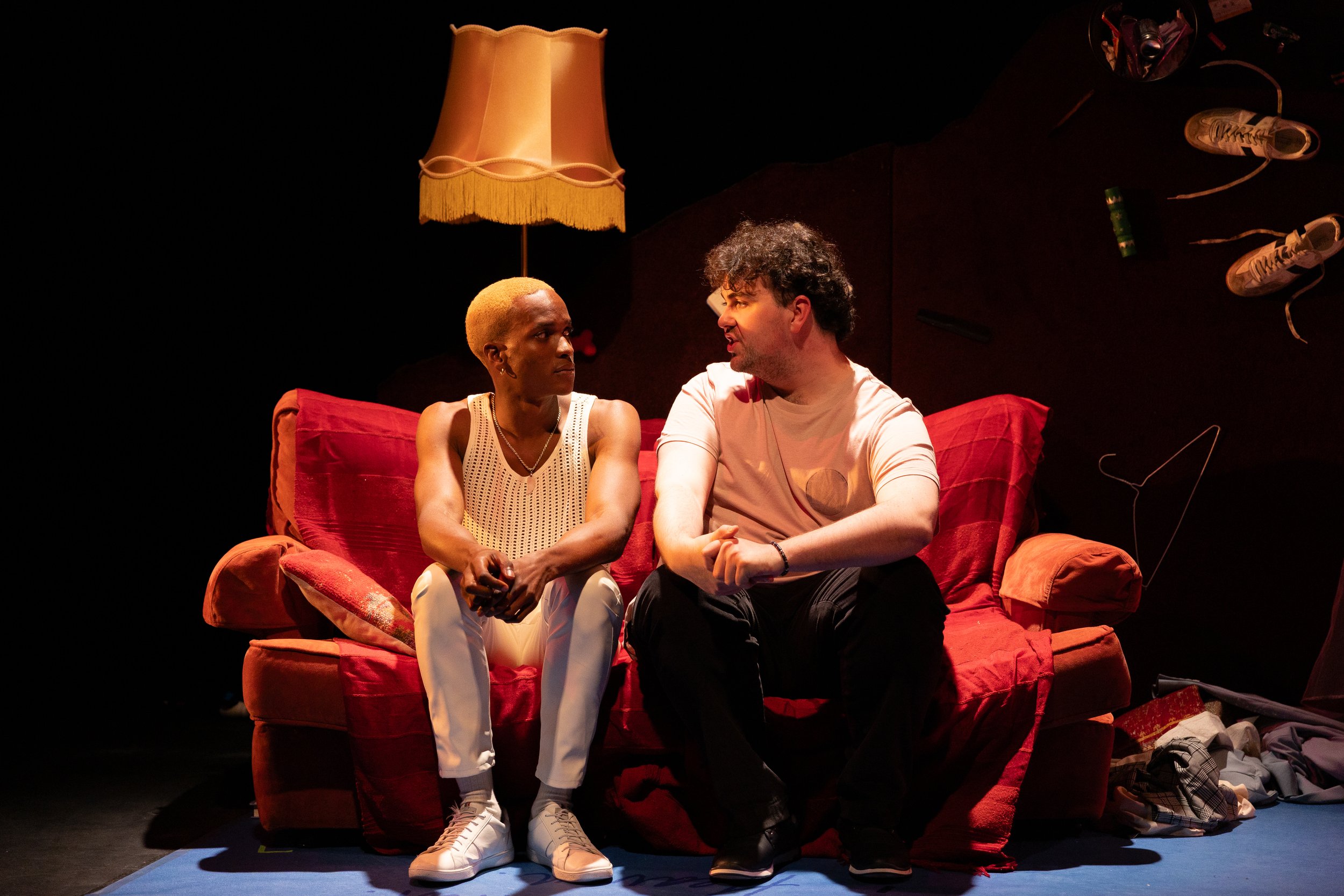 Two men look at one another on a red couch