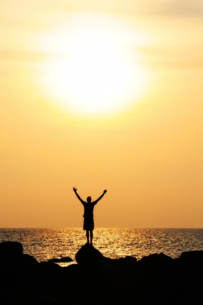 man standing on beach arms raised in victory.