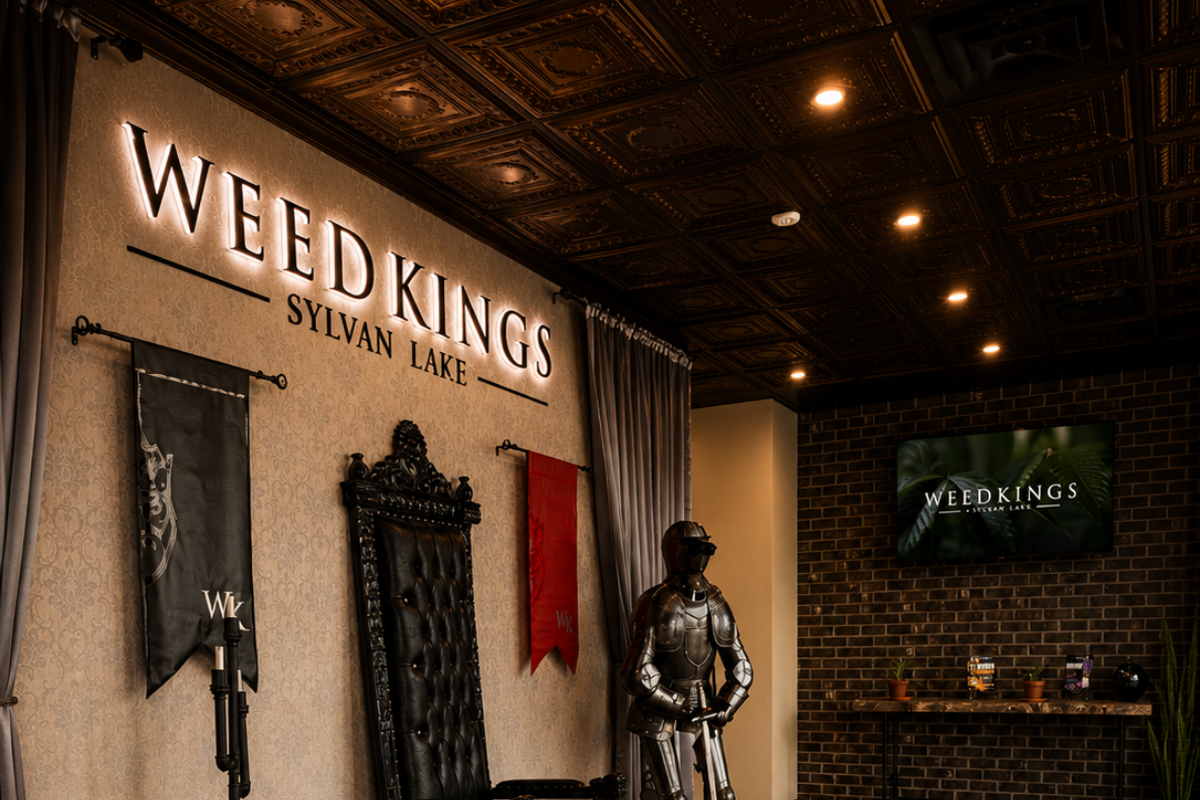 Interior of Weed Kings dispensary featuring a large wall sign, two banners, a throne-like chair, a suit of armor, and a flat-screen TV on a brick wall.