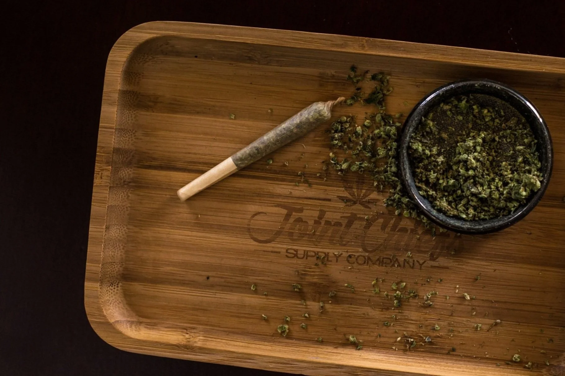 A bamboo tray with a small wooden rolling pin and a black bowl filled with chopped herbs, with some herbs scattered on the tray.