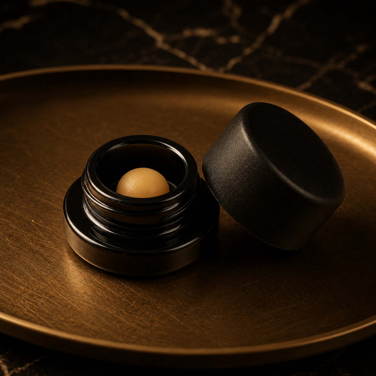 A black jar with a cannabis concentrate inside on a gold metal tray