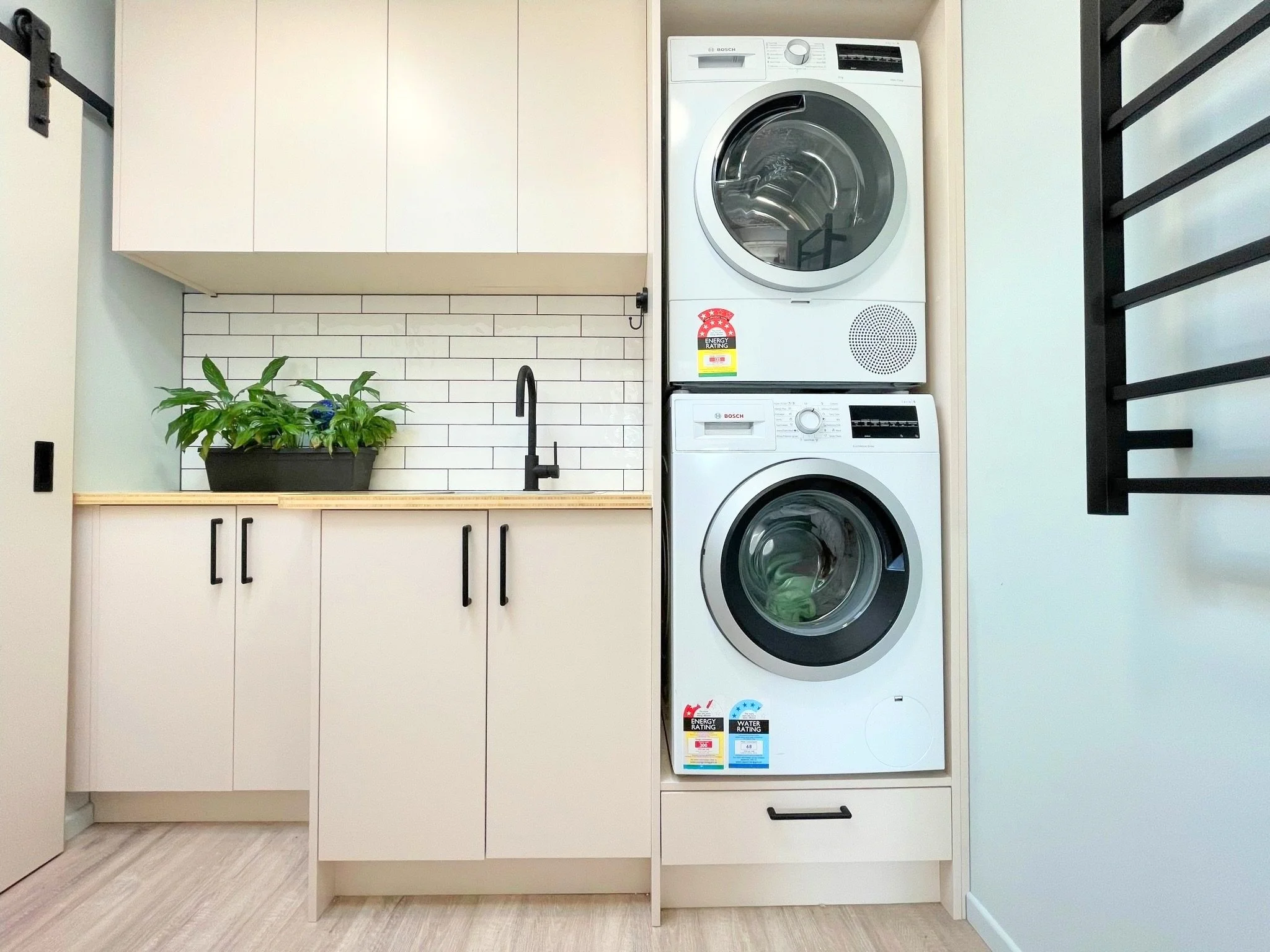 Overview of laundry with stacked washer and dryer, pink cabinetry and white subway tile