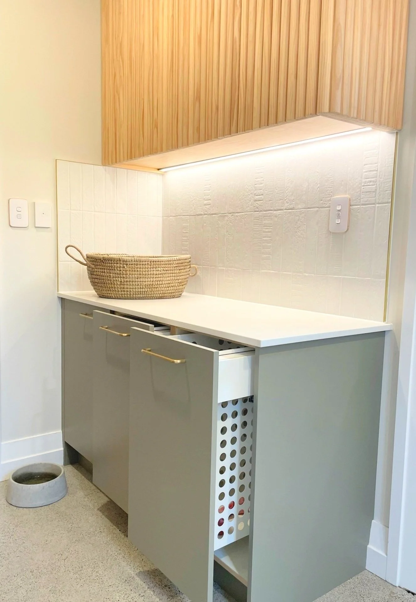 Green laundry cabinetry with pine upper cabinets. Pull out laundry basket