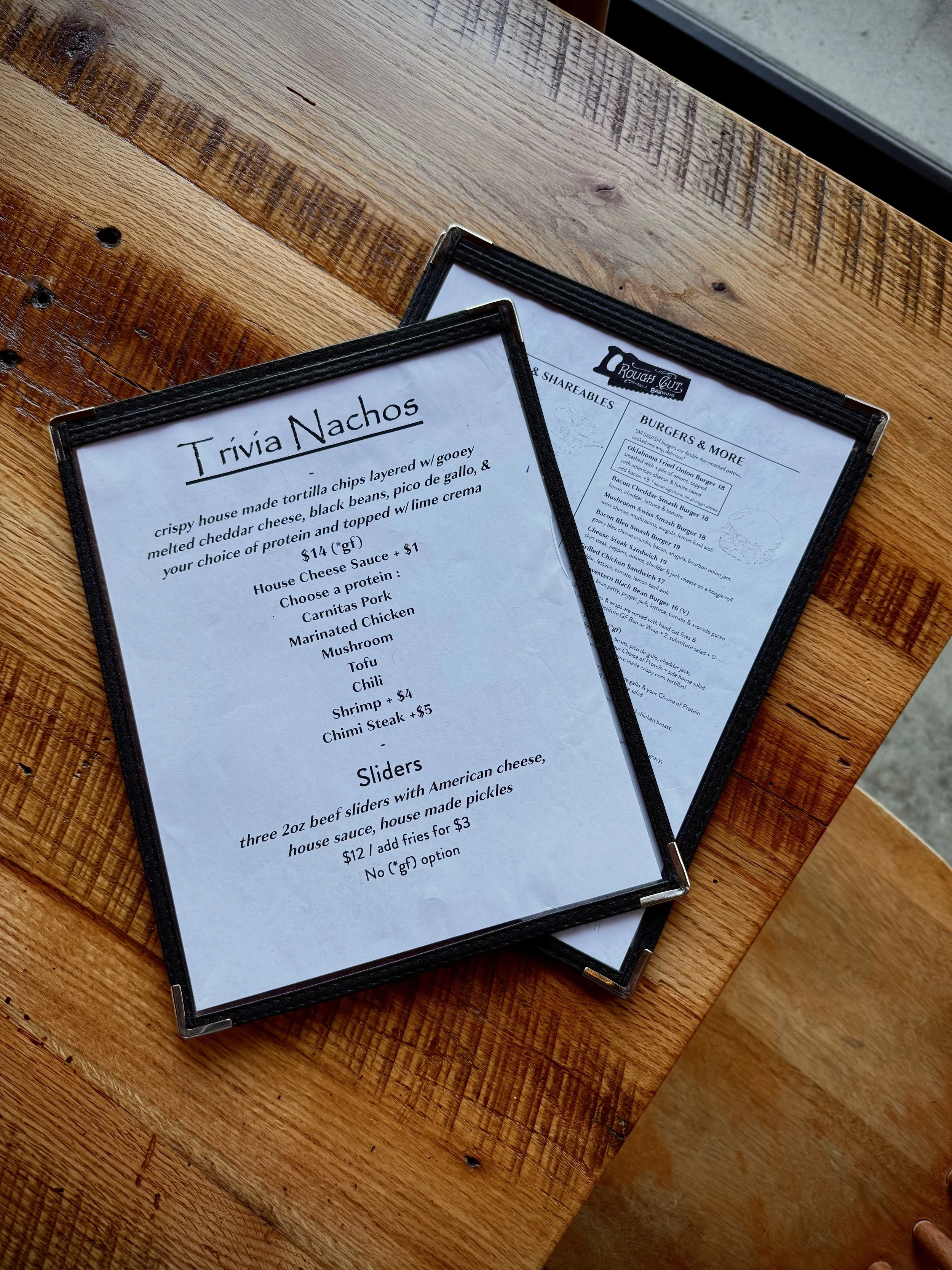 Restaurant menu featuring Trivia Nachos and sliders on a wooden table.