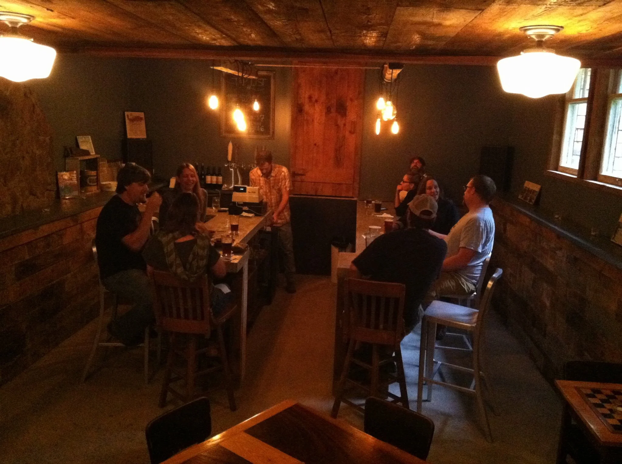 A group of people socializing in a cozy, dimly-lit pub or bar with wooden decor, tables, and warm lighting fixtures.