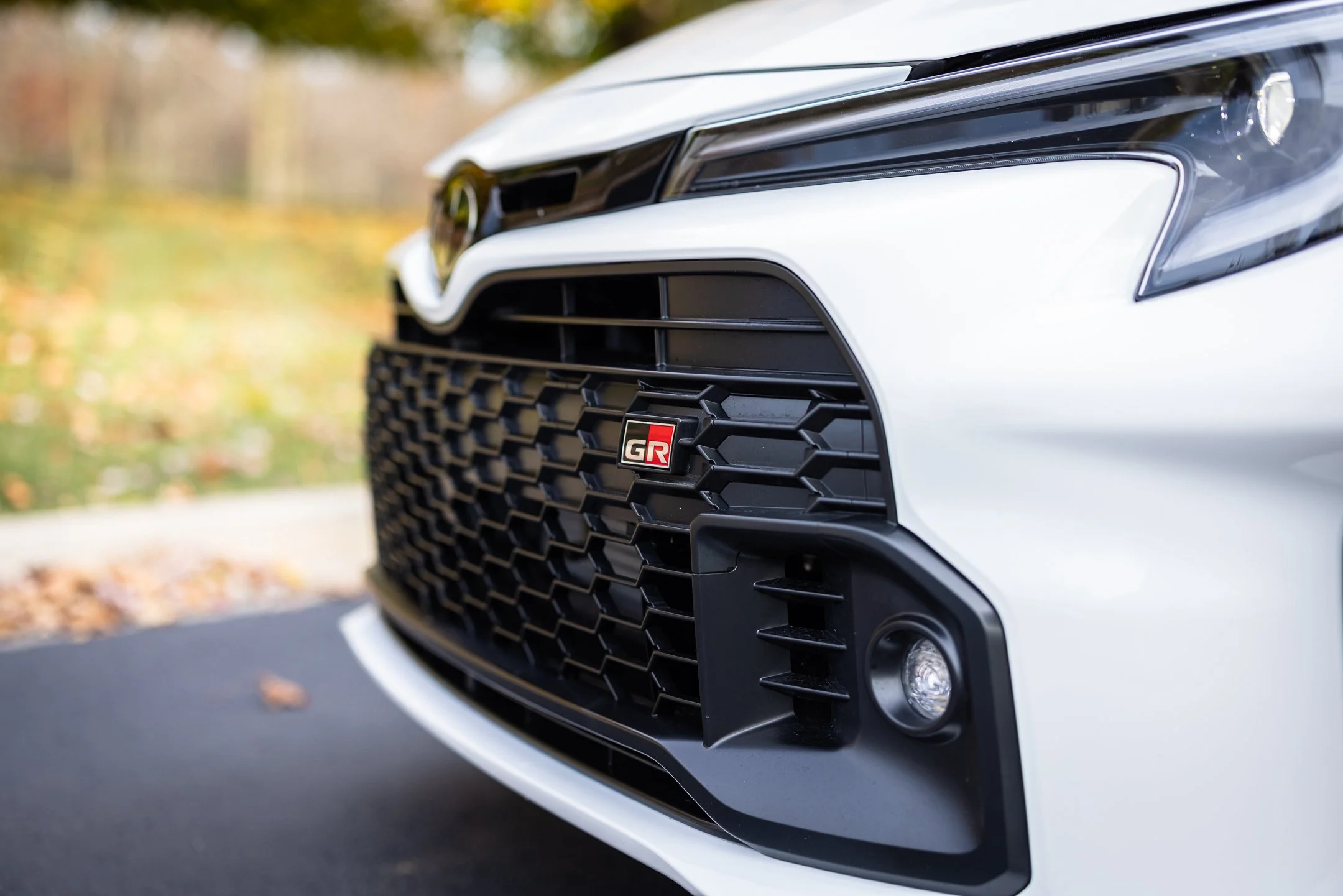 Close-up of the white Toyota GR Corolla’s front grille, GR badge, Toyota emblem, and headlight.
