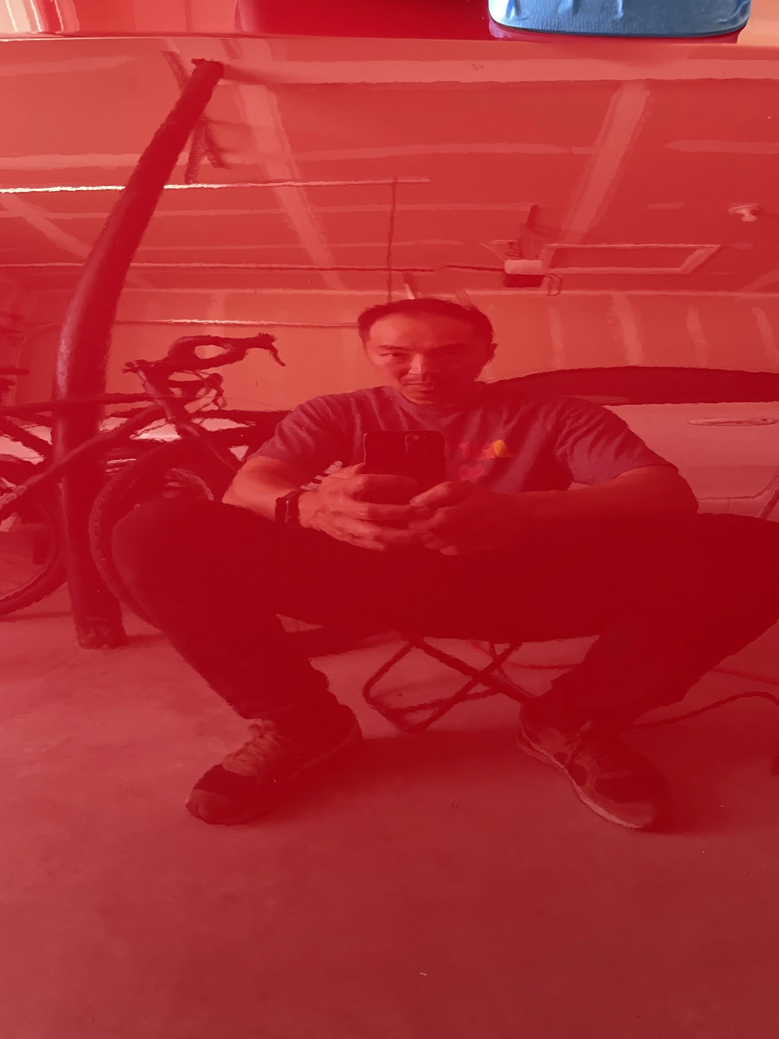 A person seated in the garage reflected in the glossy red paint of the FR-S.