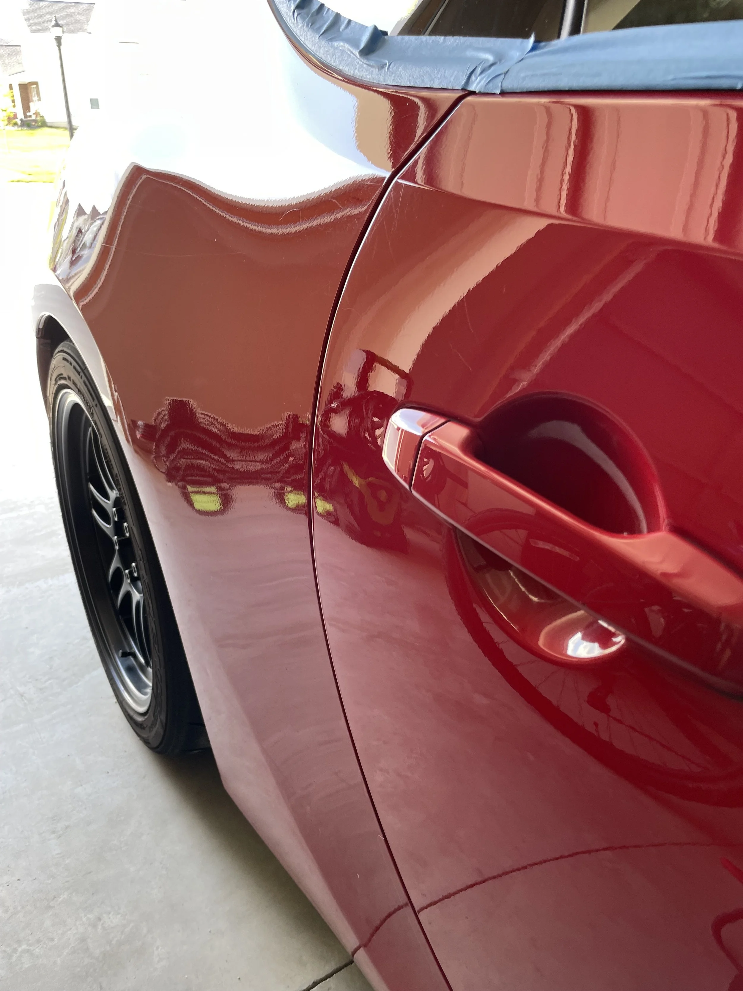 Glossy red FR-S door and handle reflecting the garage and a nearby wheel.