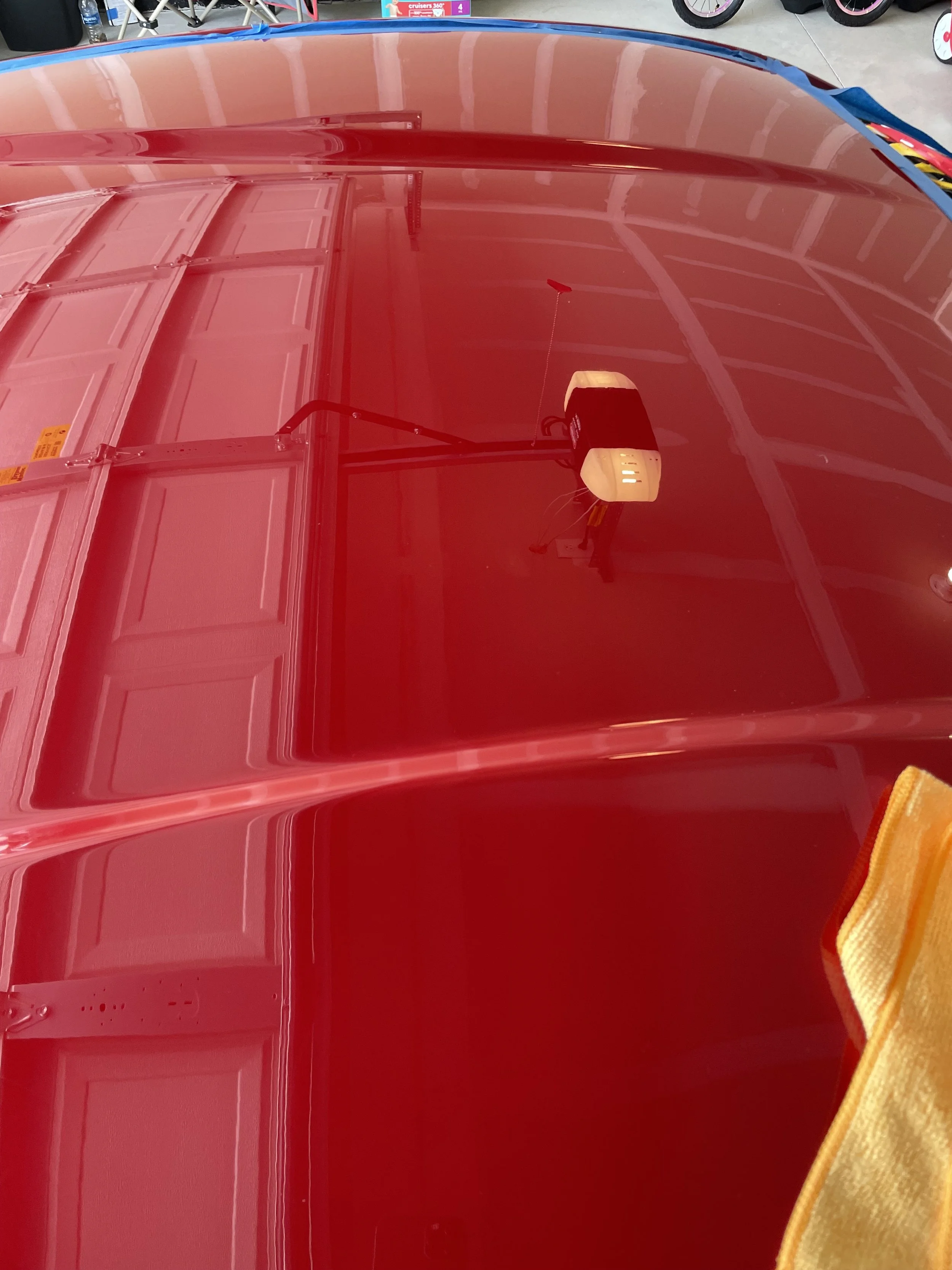 Red FR-S hood reflecting the garage door, with blue masking tape and a yellow microfiber towel.