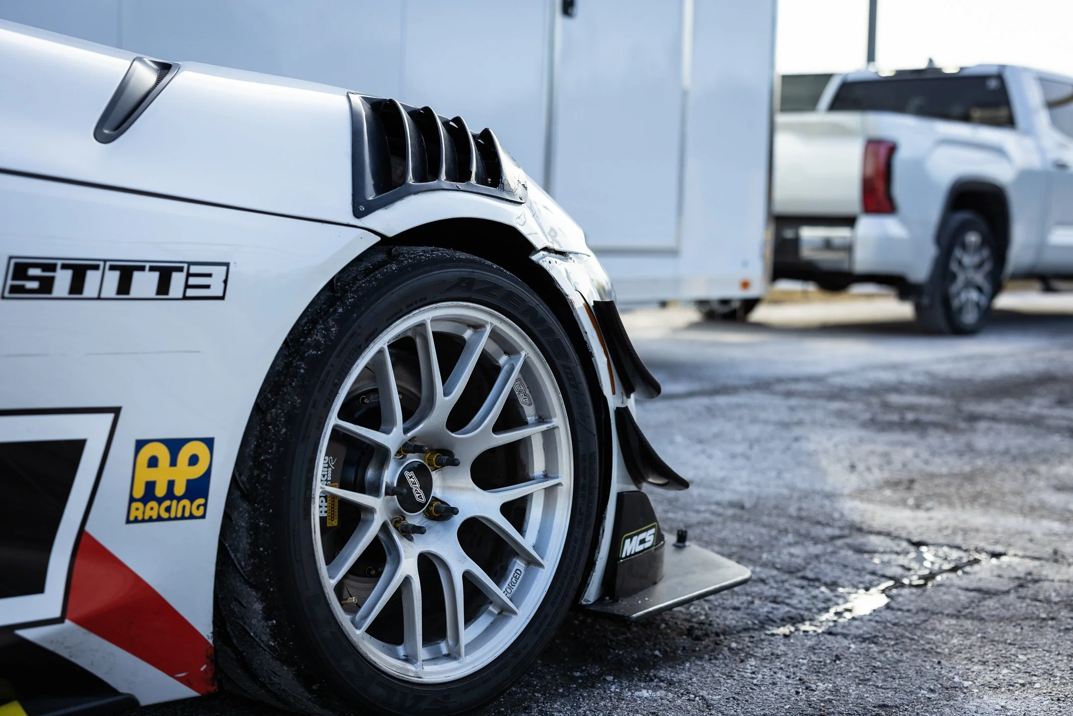 Close-up of the Toyota GR Supra race car’s front wheel, AP Racing brake caliper, fender vents, and front splitter