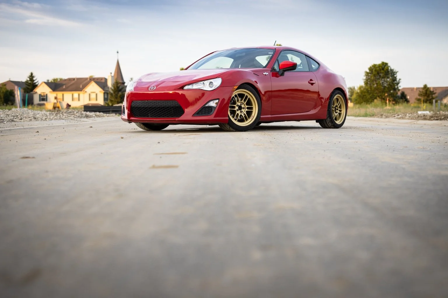 Red 2013 Scion FR-S with gold Enkei wheels, photographed from a low front three-quarter angle outdoors.