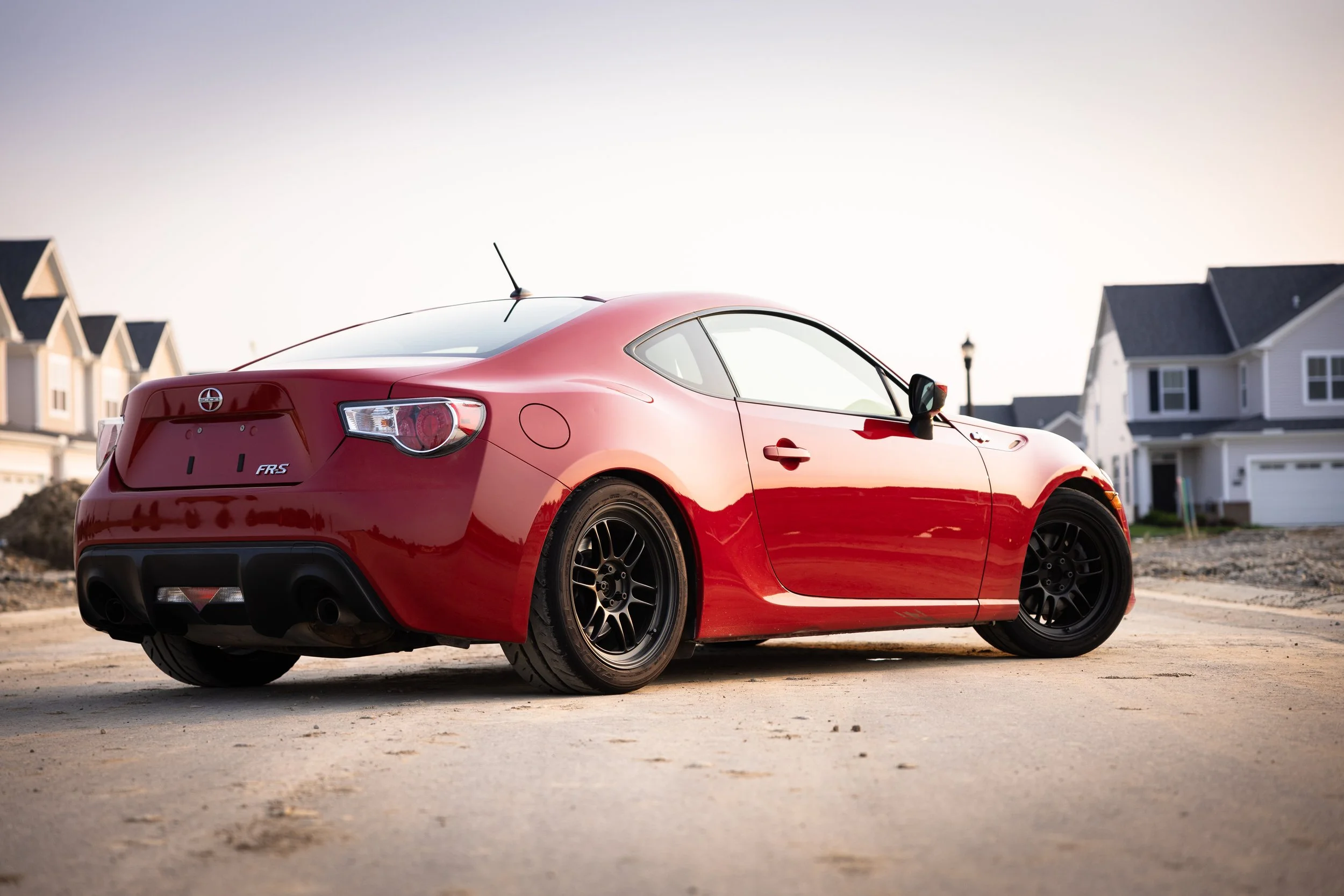 Rear three-quarter view of a glossy red Scion FR-S with dark multi-spoke wheels parked outdoors.