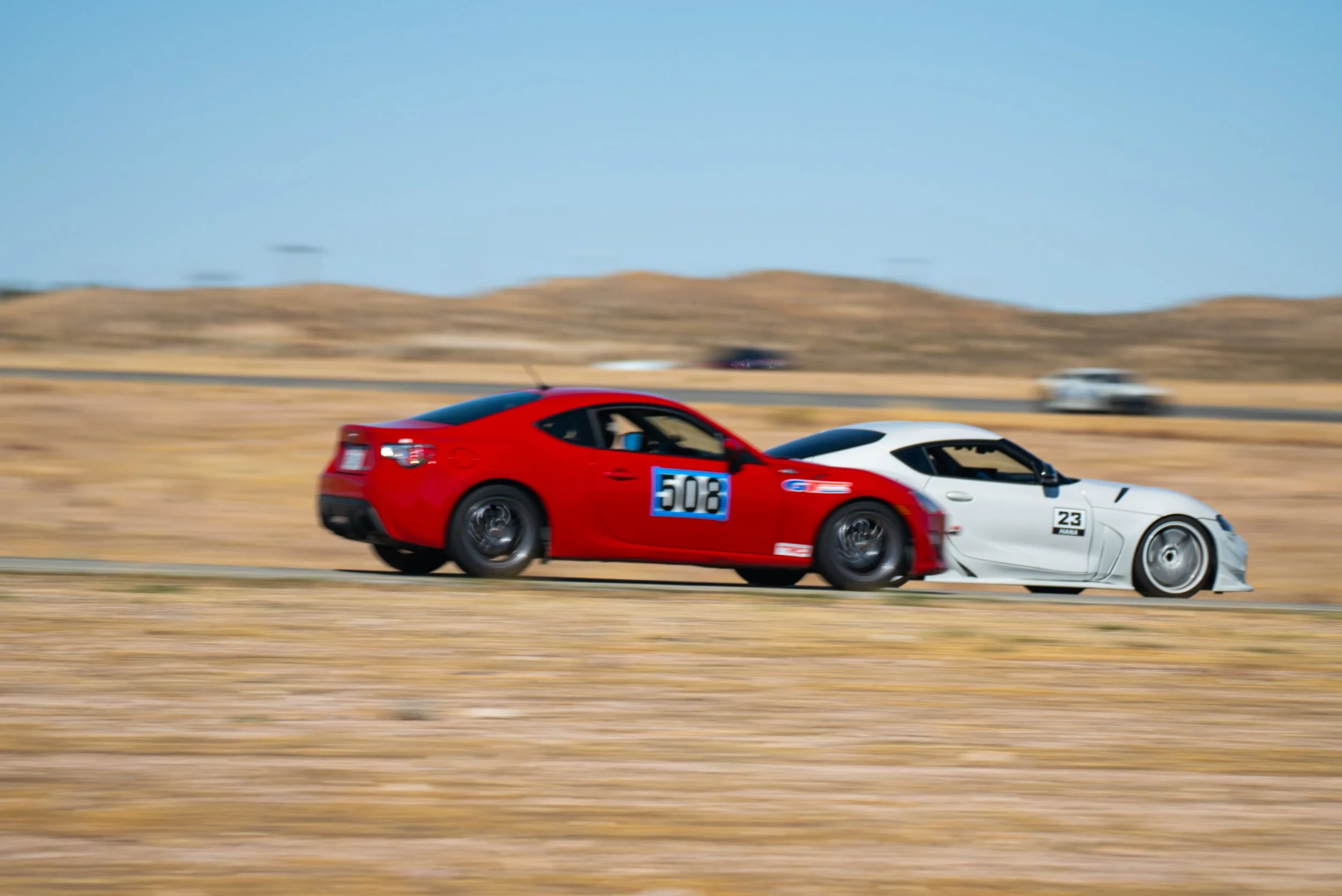 Red Scion FR-S number 508 alongside a white A90 Supra at Streets of Willow, with dry grass and low hills in the background.