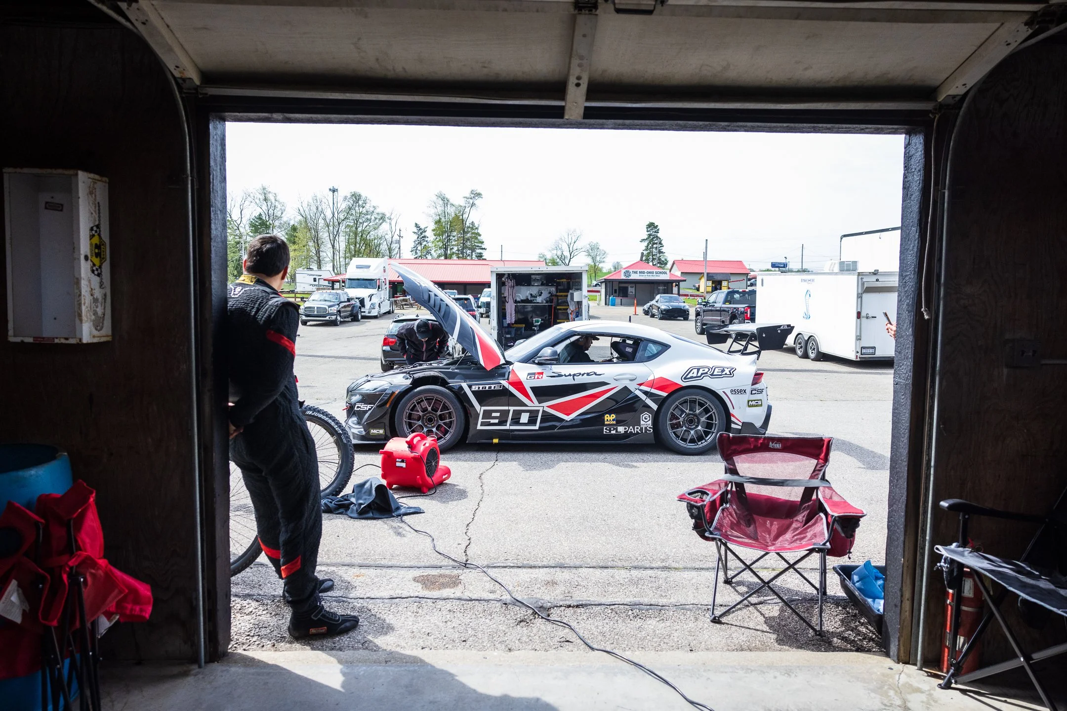 Number 90 Toyota R&D Racing A90 Supra with its hood open outside a paddock garage at Mid-Ohio.