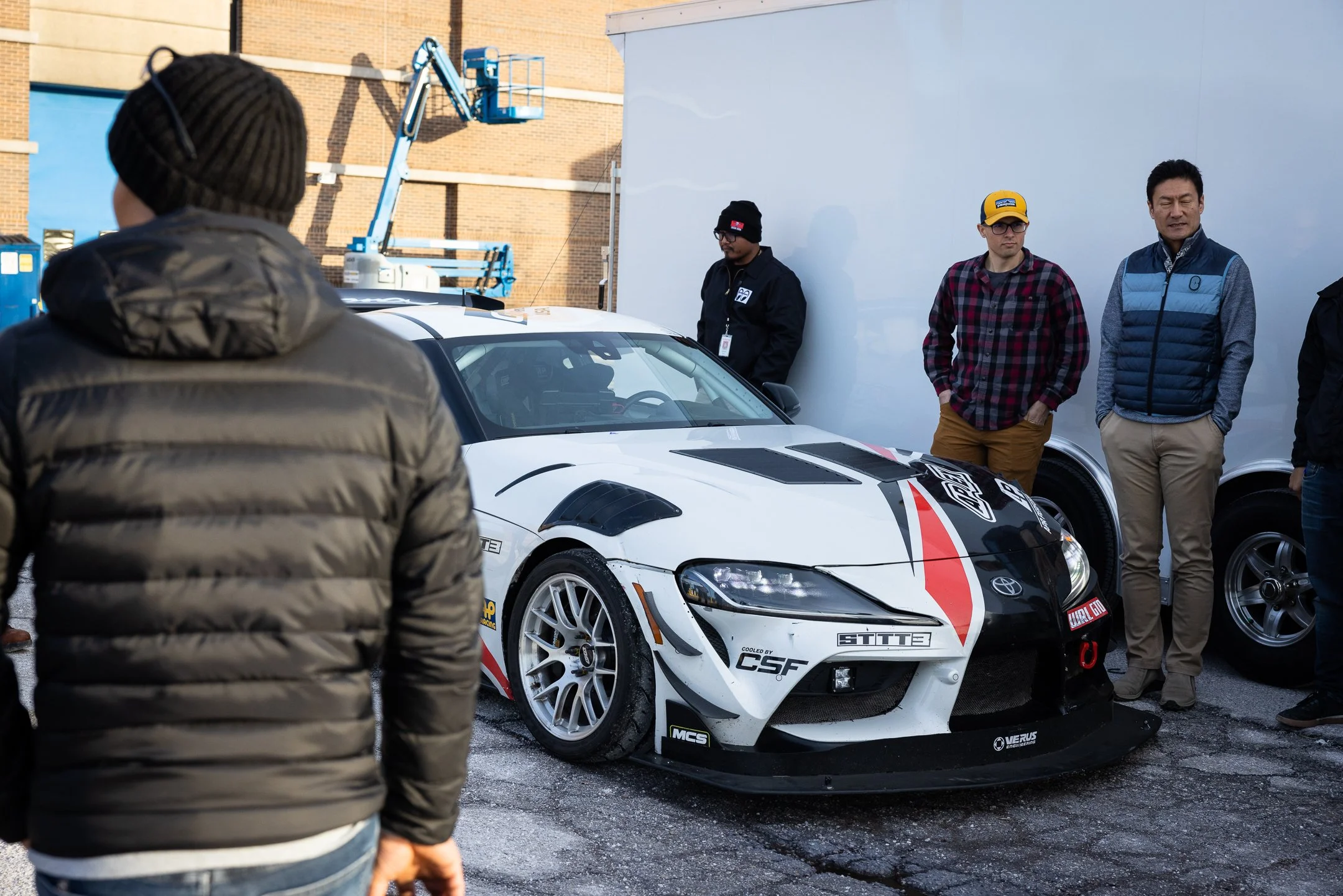 Toyota employees gathered around the A90 GR Supra race car beside its transport trailer in Michigan
