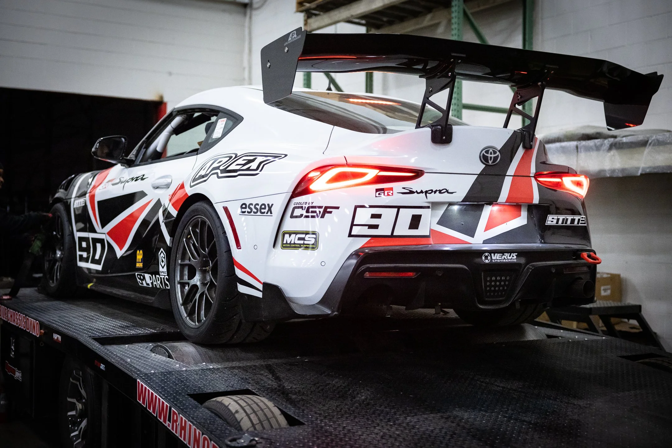 Rear three-quarter view of the number 90 Toyota GR Supra race car on the chassis dyno at Rhino Dyno in Novi, Michigan
