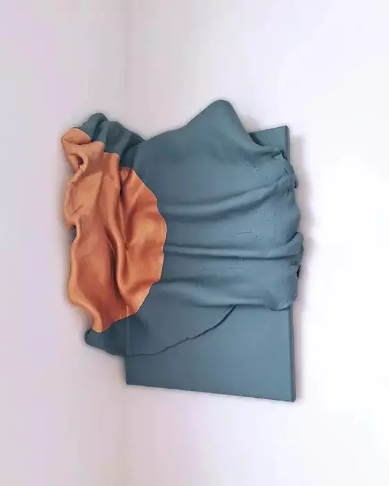 An abstract mixed media artwork featuring a blue and orange fabric piece mounted on a wall.