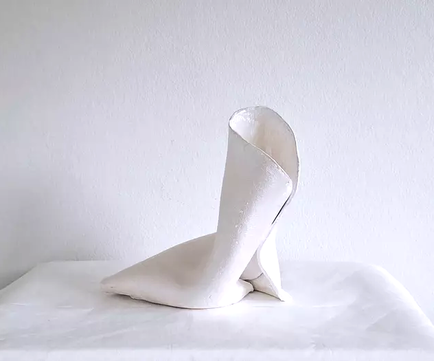 Minimalist white ceramic sculpture of a high-heeled shoe on a white surface.
