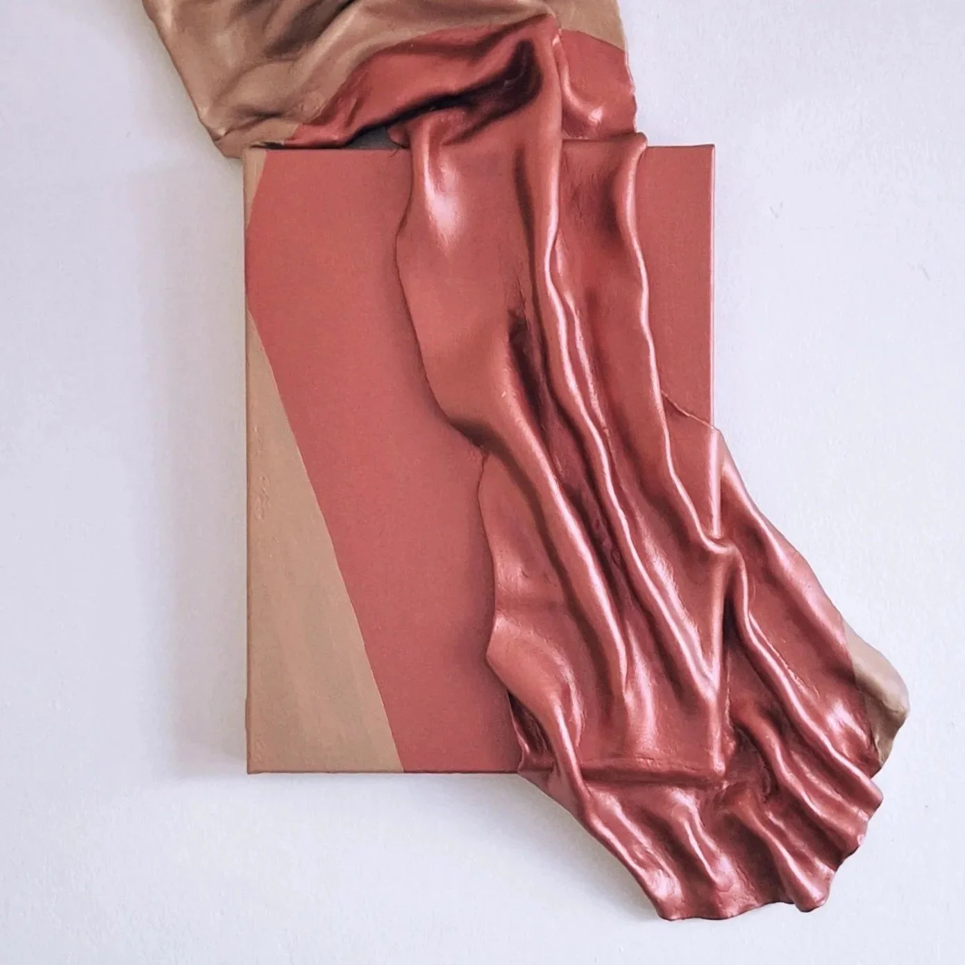 Mixed media art piece combining a painted rectangle and metallic, draped, clay-like material on white wall.