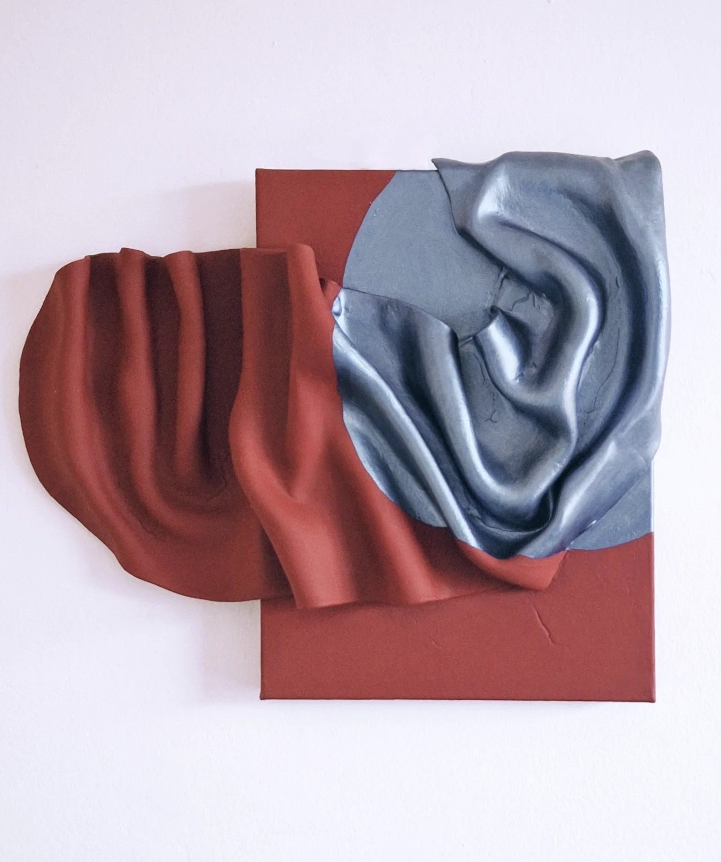 Mixed media artwork featuring a red draped clay folds on the left and a metallic sheen resembling the moon on the right, mounted on a red rectangular base.