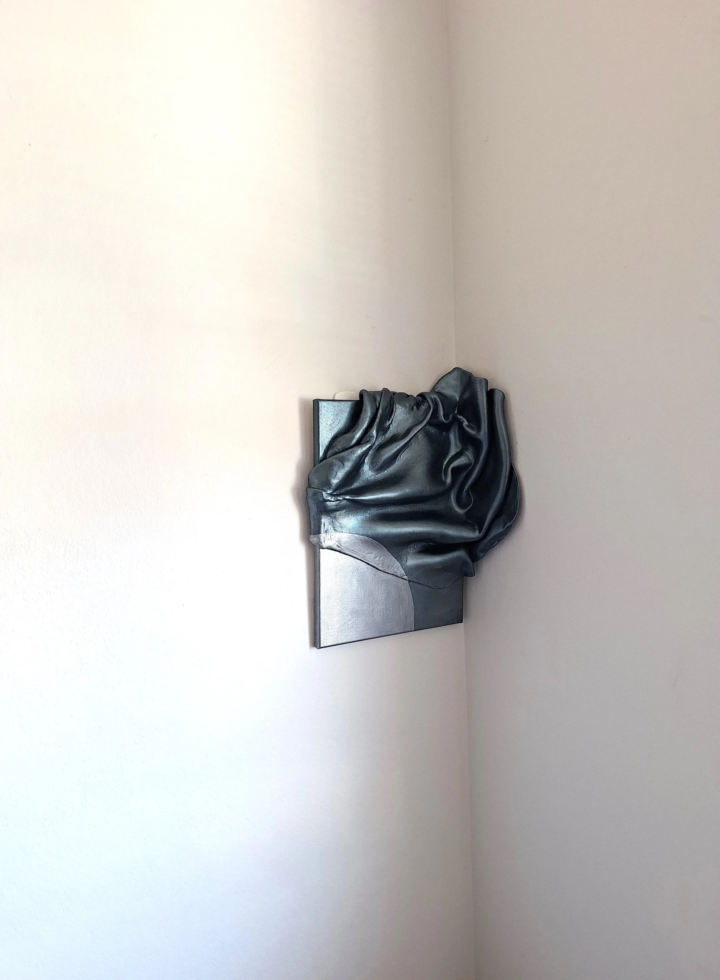 A modern abstract sculpture of a draped clay that appears like fabric on a rectangular canvas, placed against a plain white wall.
