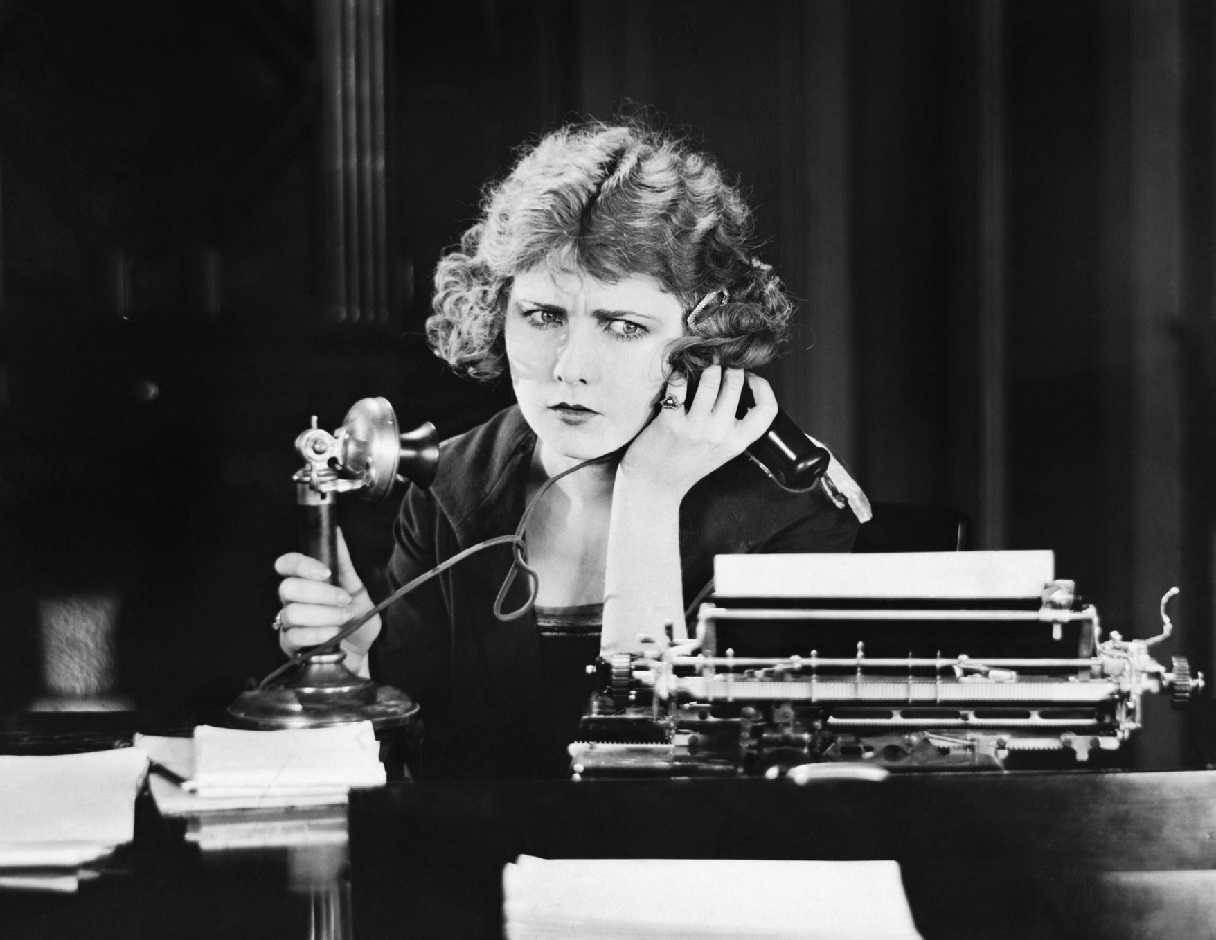 black and white photo of a woman with a short curled bob haircut on old fashioned landline phone  with a confused or frustrated expression on her face. ©The Everett Collection via Canva.com