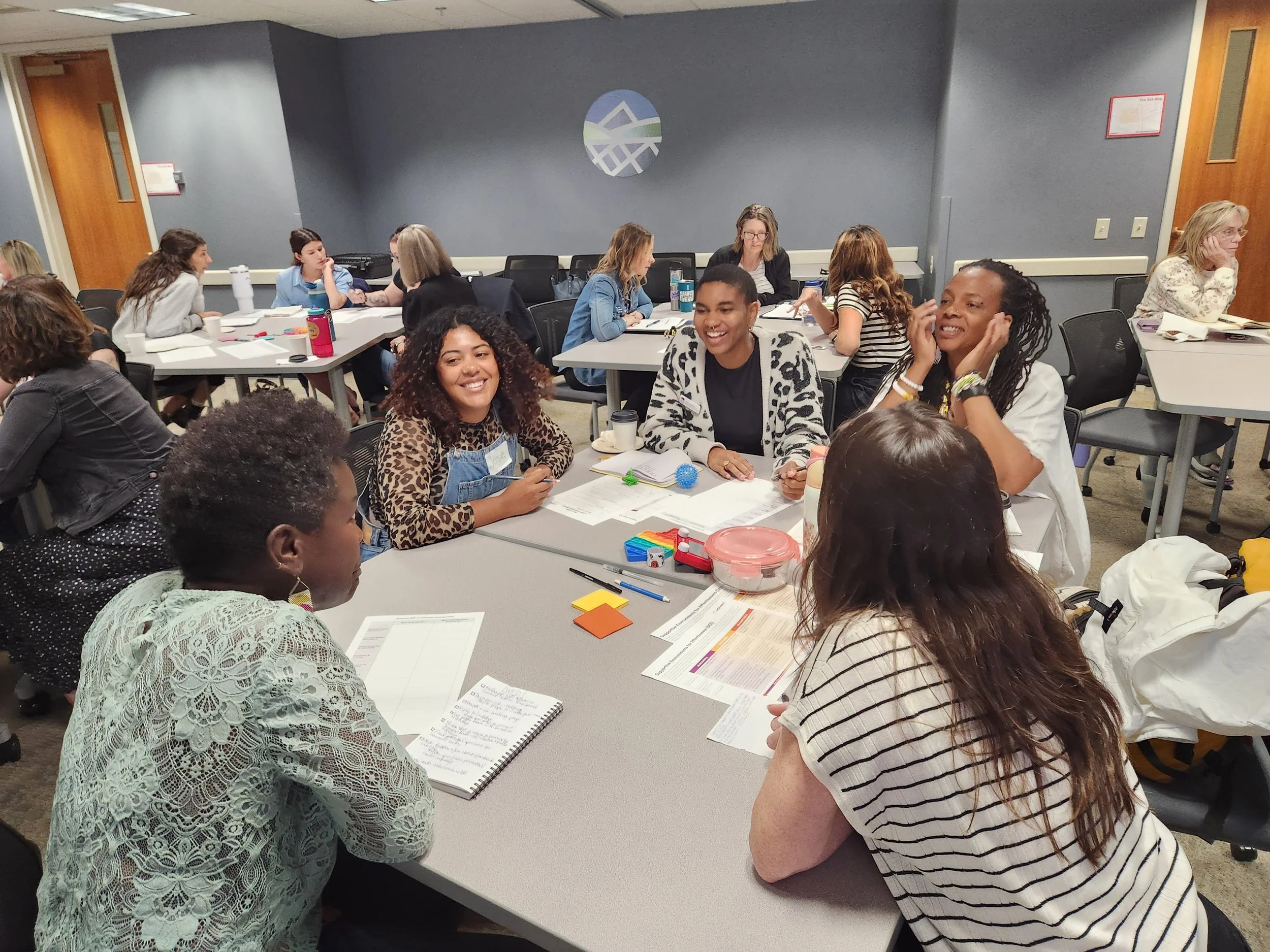 group of smiling women sitting at a round table. working together to learn the SEE framework