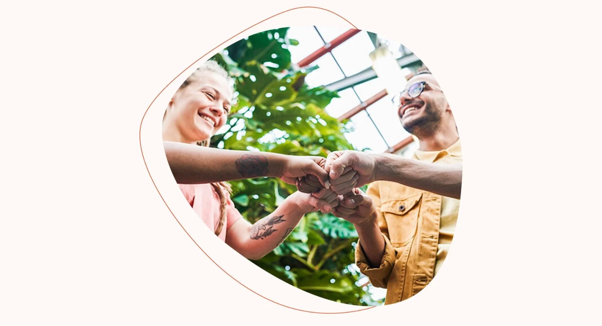 Two people smiling and shaking hands in a greenhouse surrounded by large green plants.