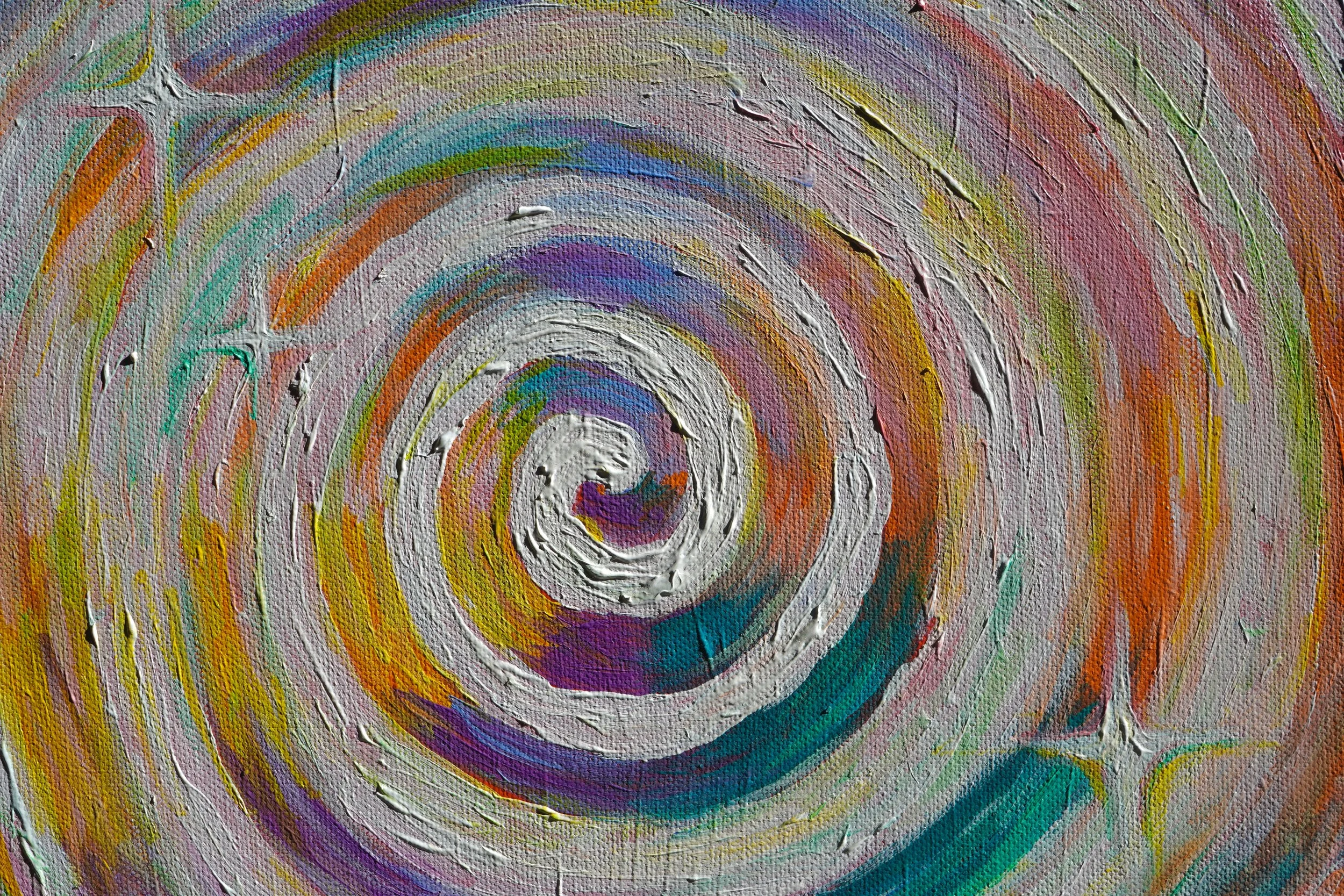A close-up photograph of a textured canvas painting featuring colorful concentric circles and swirling patterns in shades of purple, blue, green, yellow, orange, and white.
