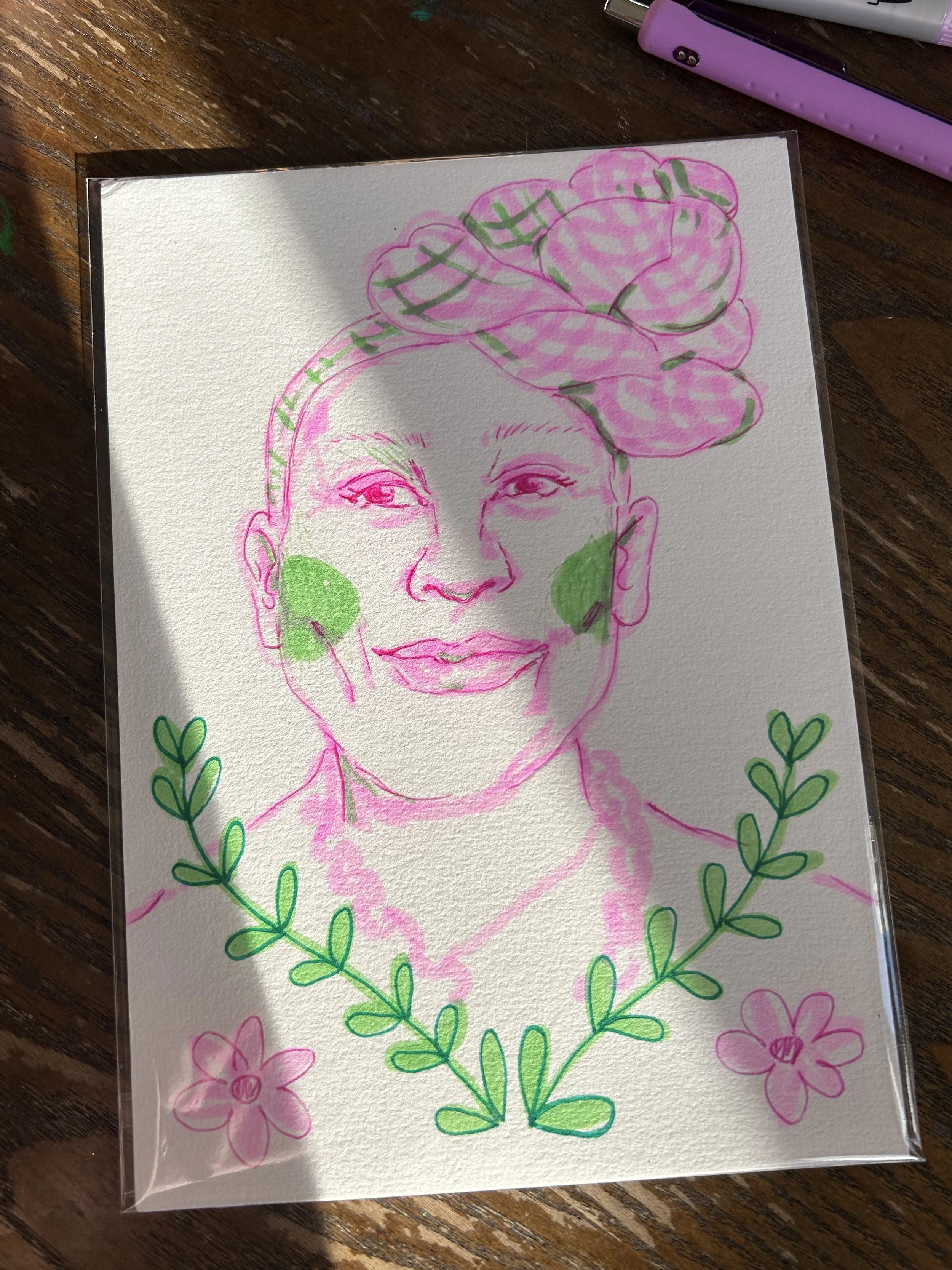 A colorful drawing of a woman with pink and green accents, surrounded by green leaves and pink flowers. The artwork appears to be made with pastel or marker on textured paper, with a shadow cast on the paper.