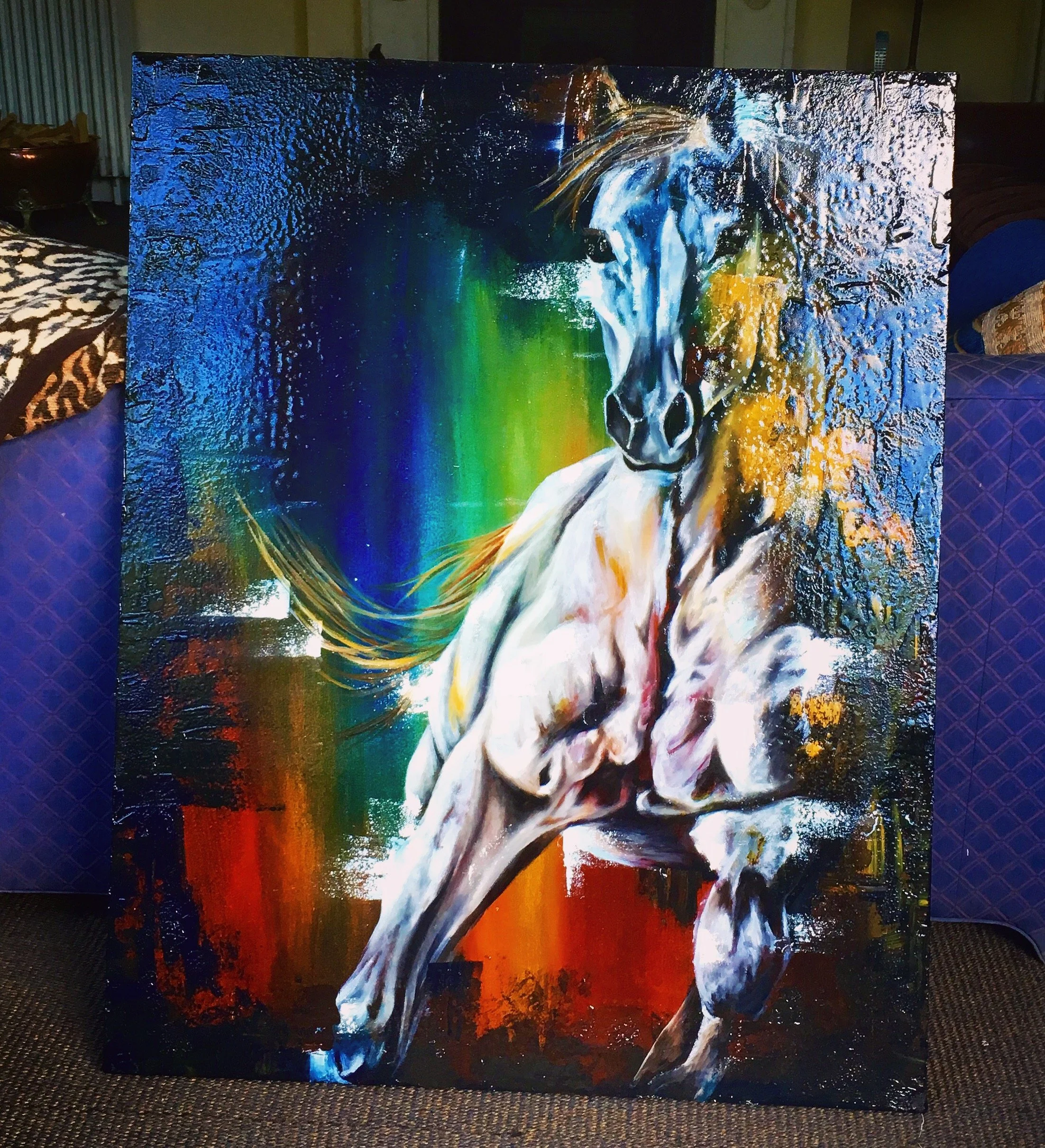 A vibrant, colorful painting of a white horse with a flowing mane, set against a background blending blue, green, red, and yellow hues. By Nicole Vanner.