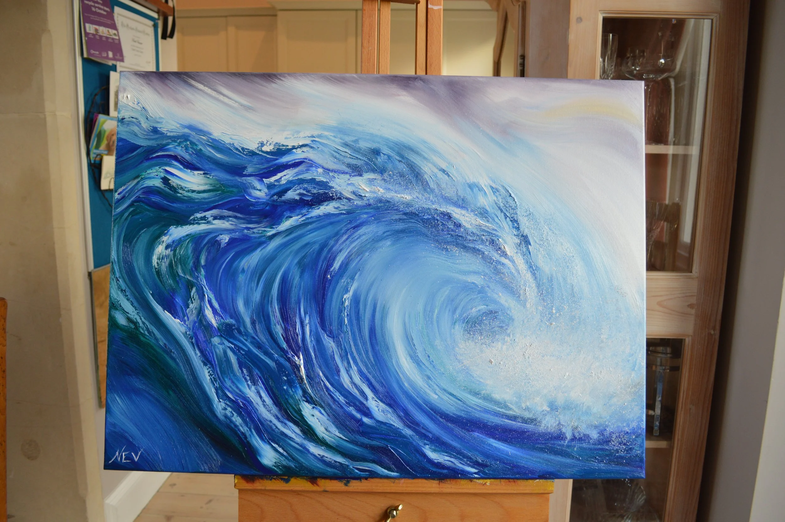 Painting of a large, blue ocean wave with white spray, swirling towards the viewer, signed by the artist 'NEV' in the bottom left corner. By Nicole Vanner.