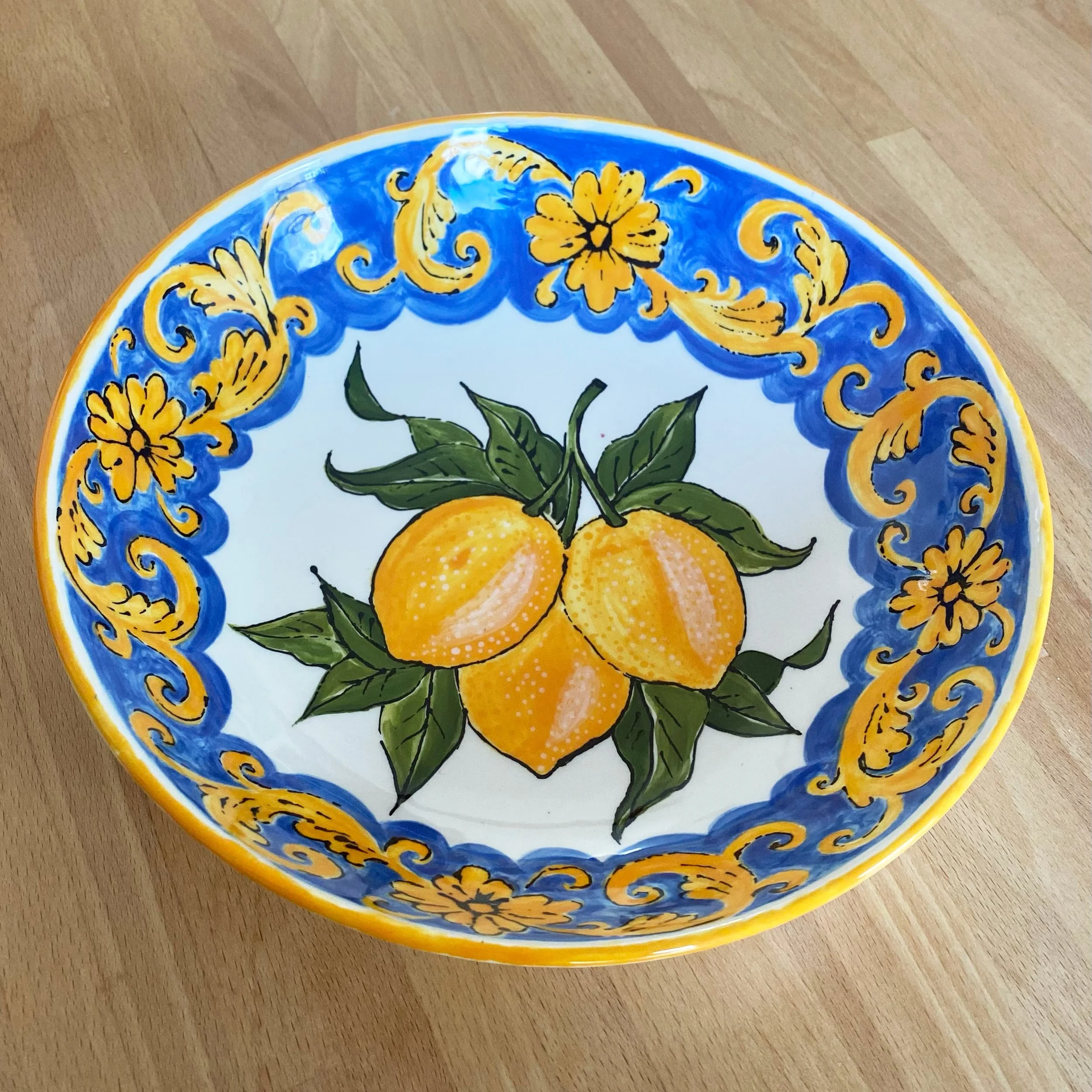 Colorful ceramic bowl decorated with lemons and green leaves, with a blue and yellow ornate border design. By Nicole Vanner.
