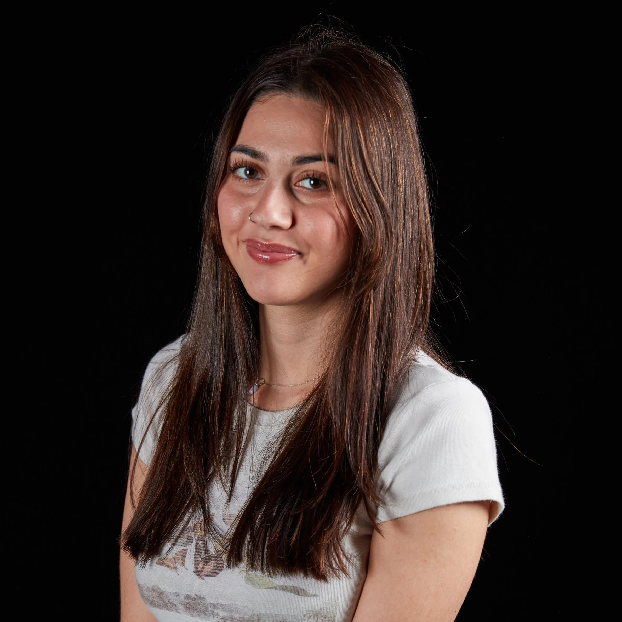 Portrait of a young woman with long brown hair, wearing a white t-shirt, against a black background.