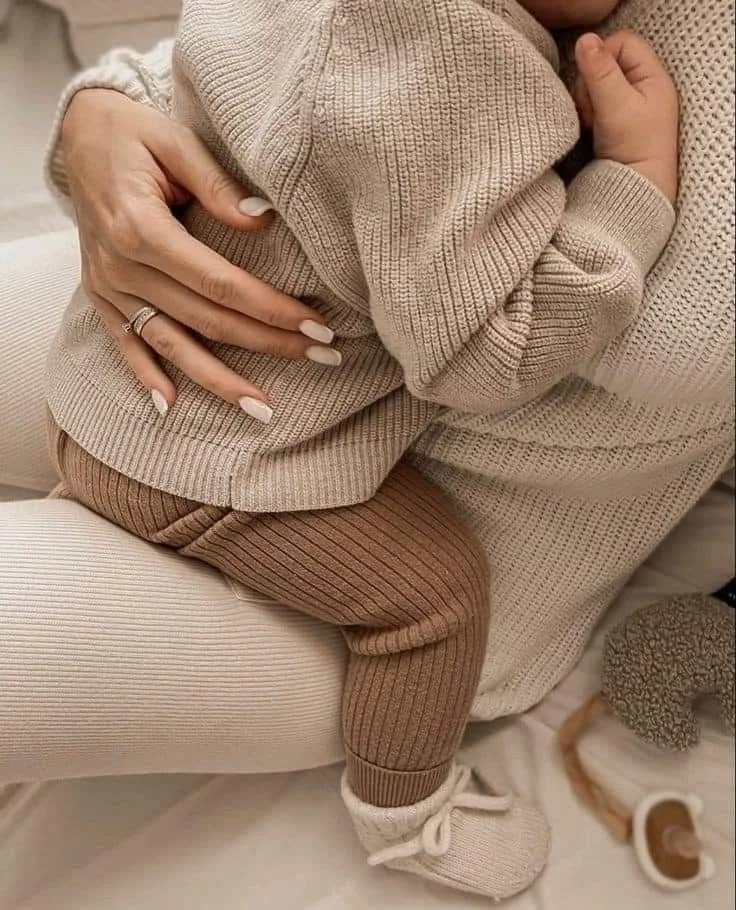 A mother holding her baby, dressed in all neutral colors