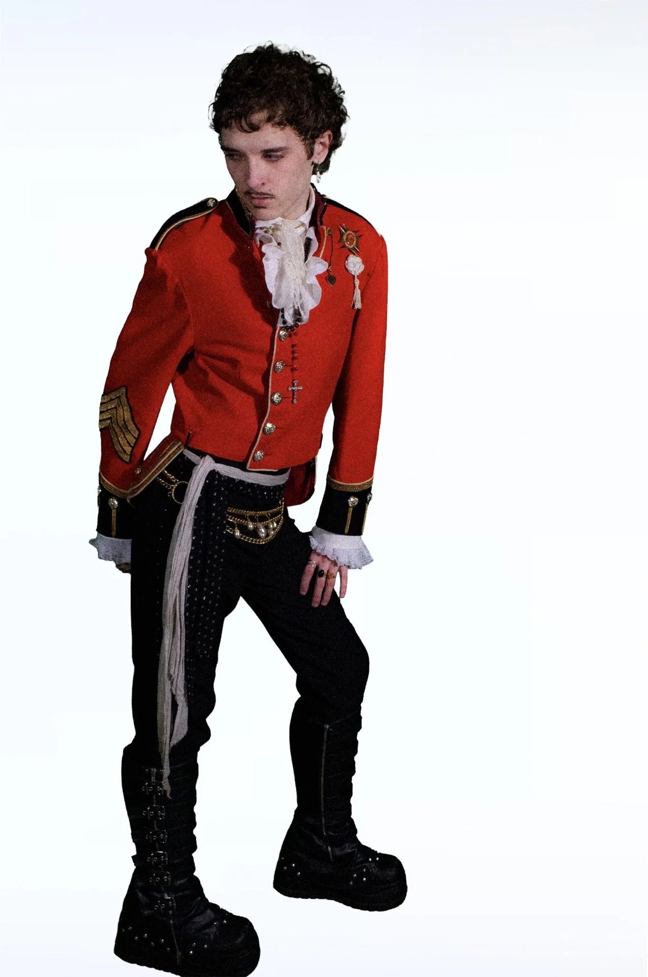      Person in a red military-style jacket and black boots standing against a white background.   