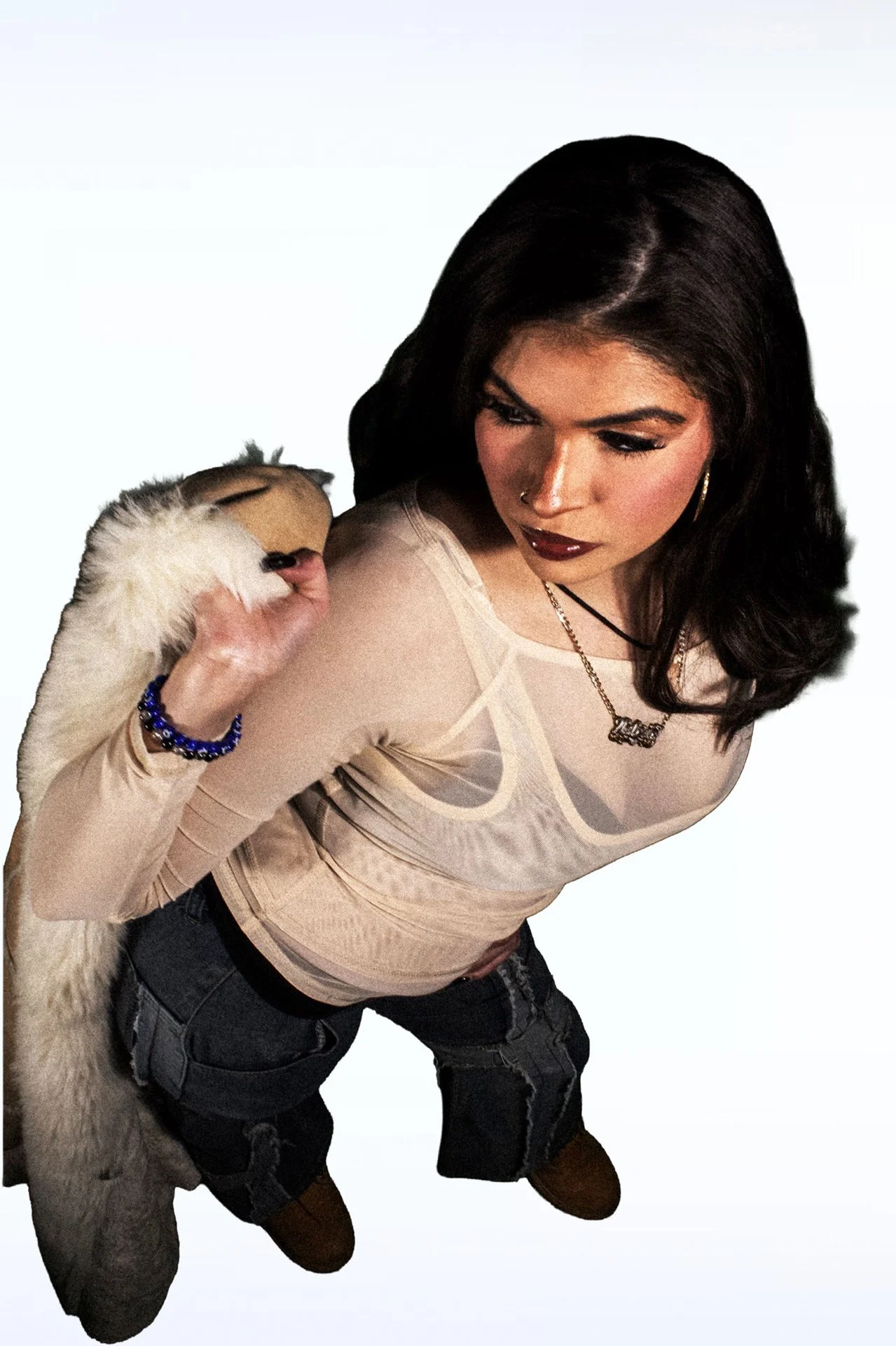  Person in a sheer top holding a fluffy jacket looking down at it against a plain background. 