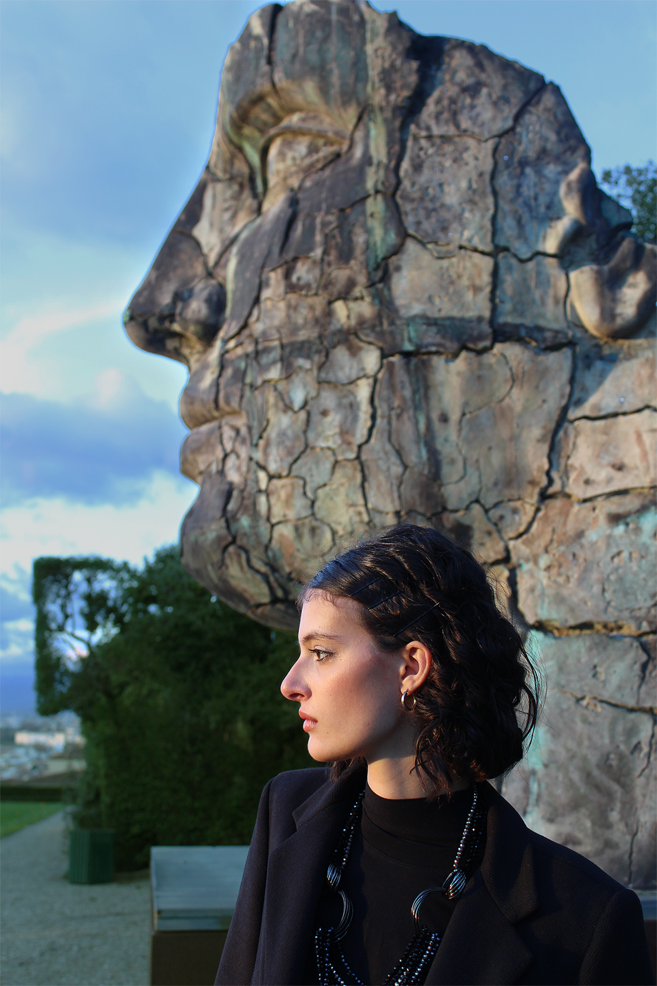 Woman side profile in front of large side profile statue outside during sunset and light is hitting the woman in a golden glow and the two figures mirror each other