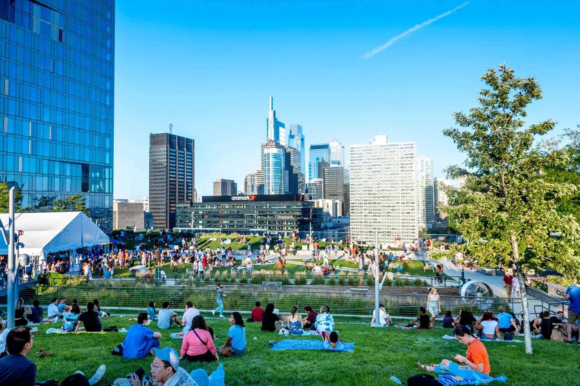 An elevated urban park featuring a large, manicured green lawn situated atop a parking garage. People are lounging on the grass and walking along paved pathways.