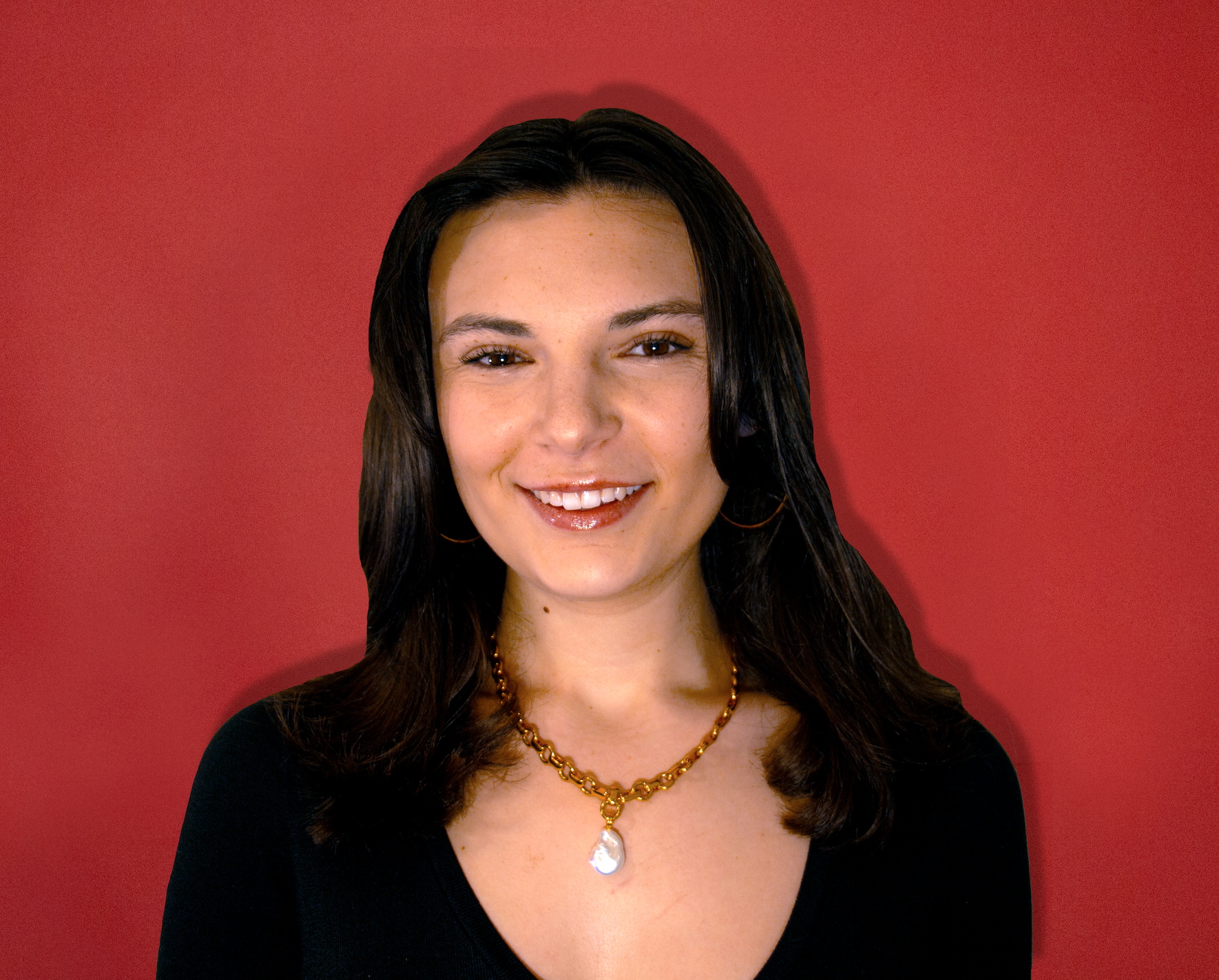 Portrait of a woman with dark hair, smiling, wearing a black top, gold necklace, and gold hoop earrings, against a red background.