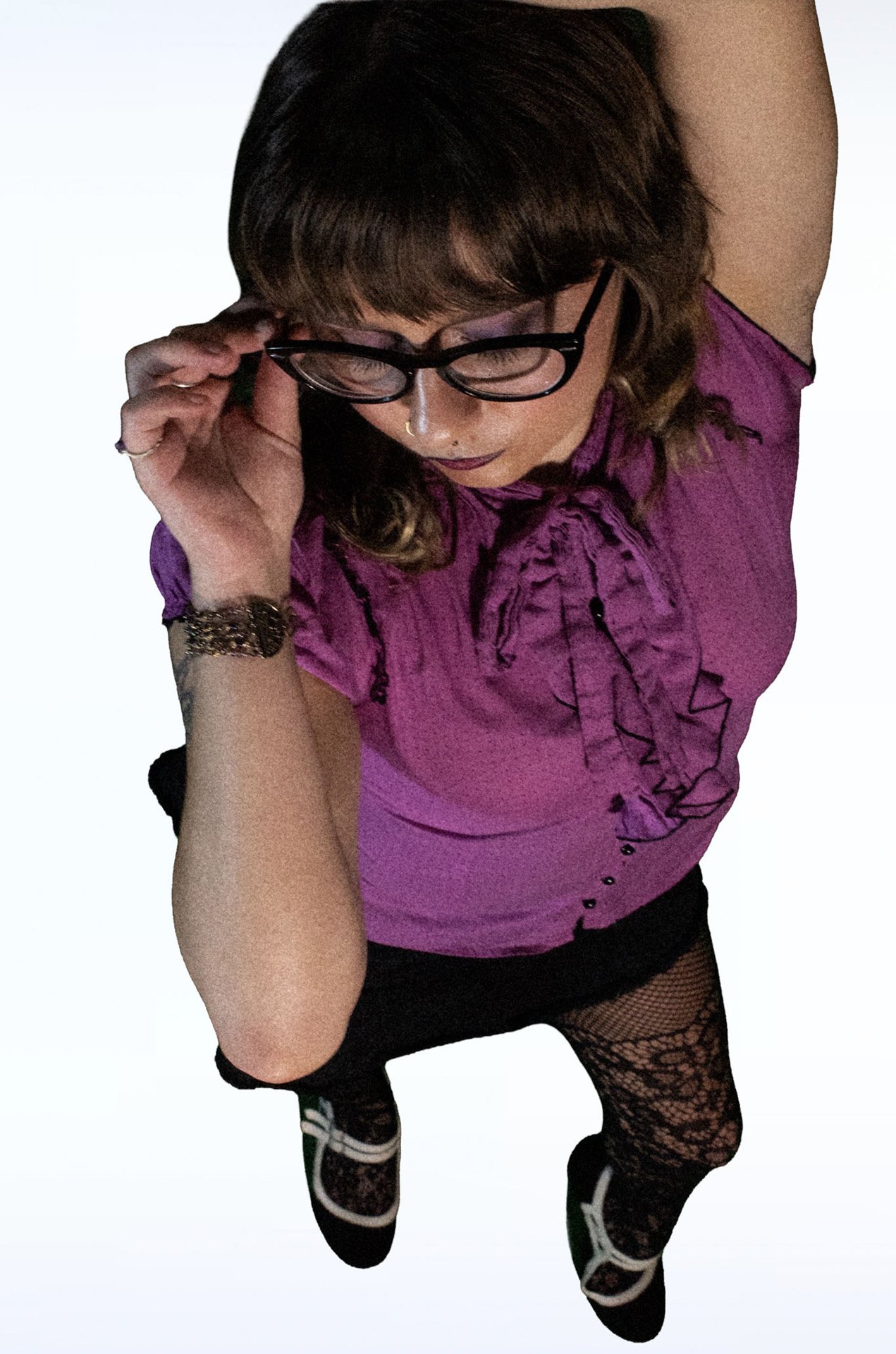 Person adjusting glasses in a purple blouse and lace tights