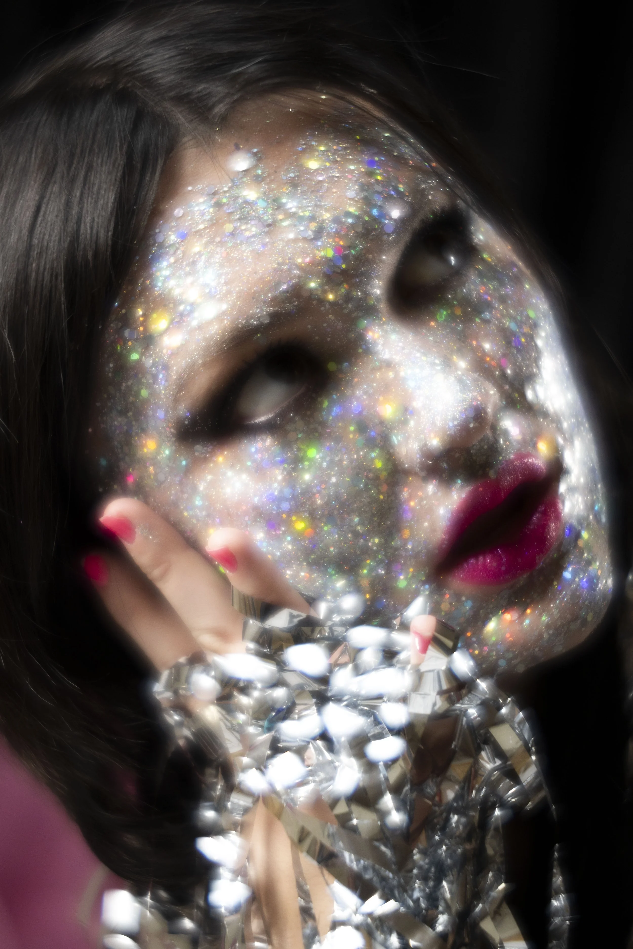 Close up photo a model with glitter all over face with pink lipstick.