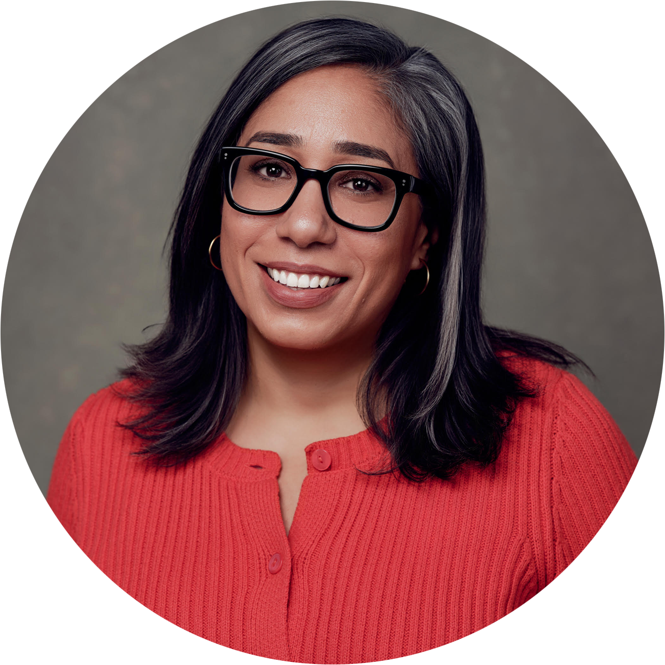 A smiling woman with long dark hair, wearing black-rimmed glasses, a red cardigan, and hoop earrings, against a neutral background.