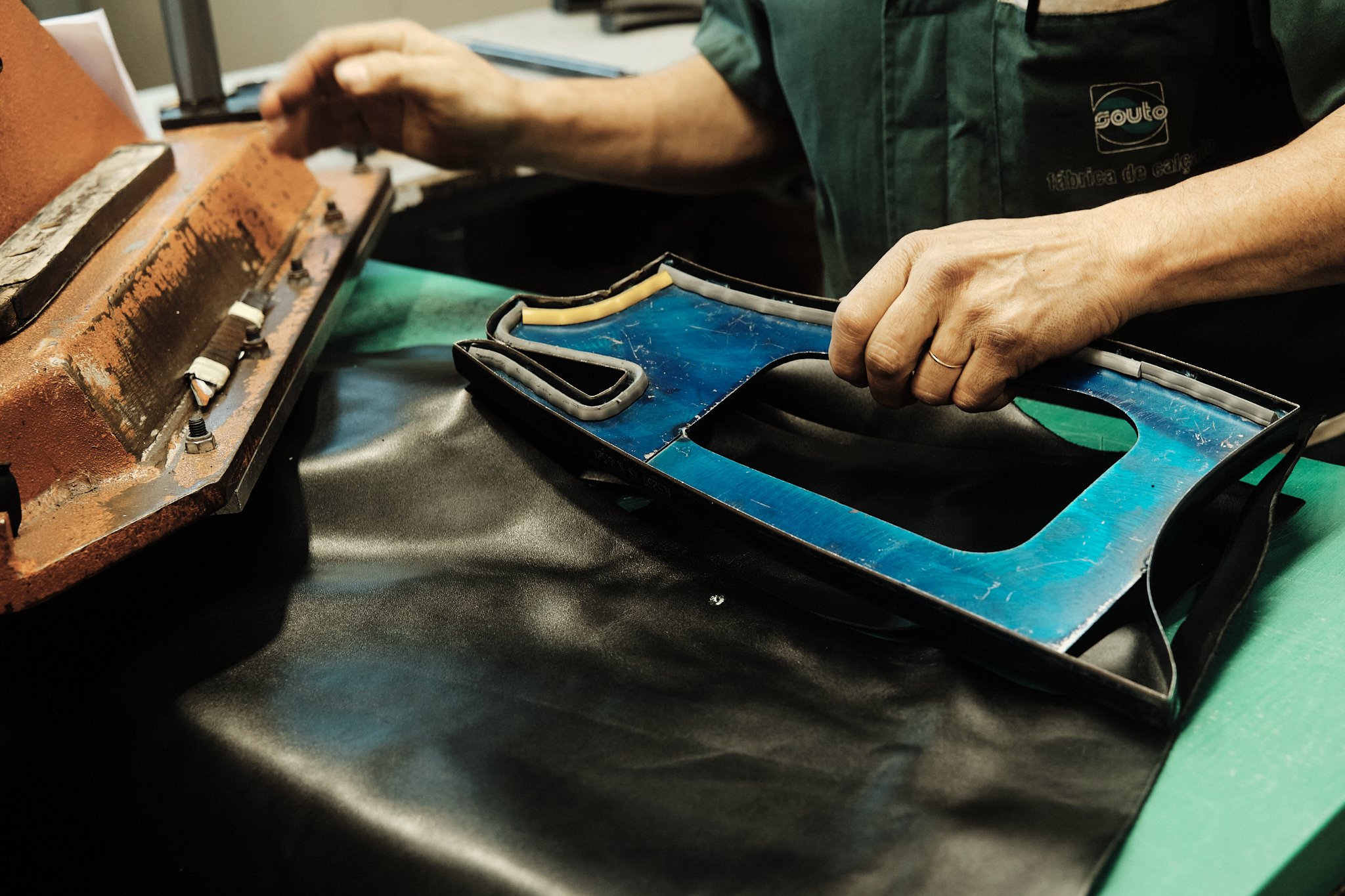 Une personne assemble une enseigne lumineuse avec des lettres en métal et une structure en plastique bleu, sur un plan de travail. La personne porte un uniforme vert.