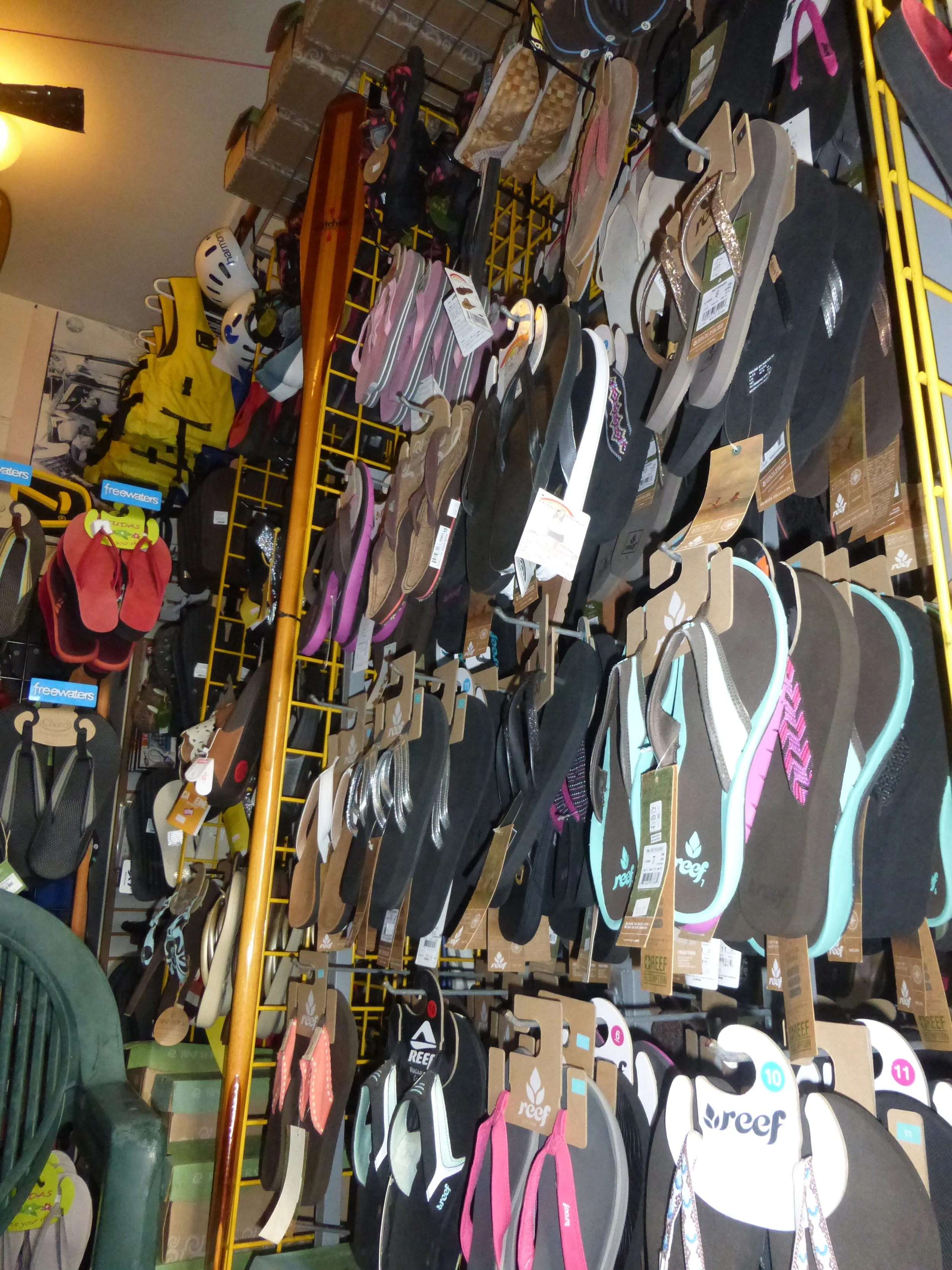 Retail store wall displaying a variety of flip-flops and sandals on hooks. Chaco, Rainbow, Reefs.