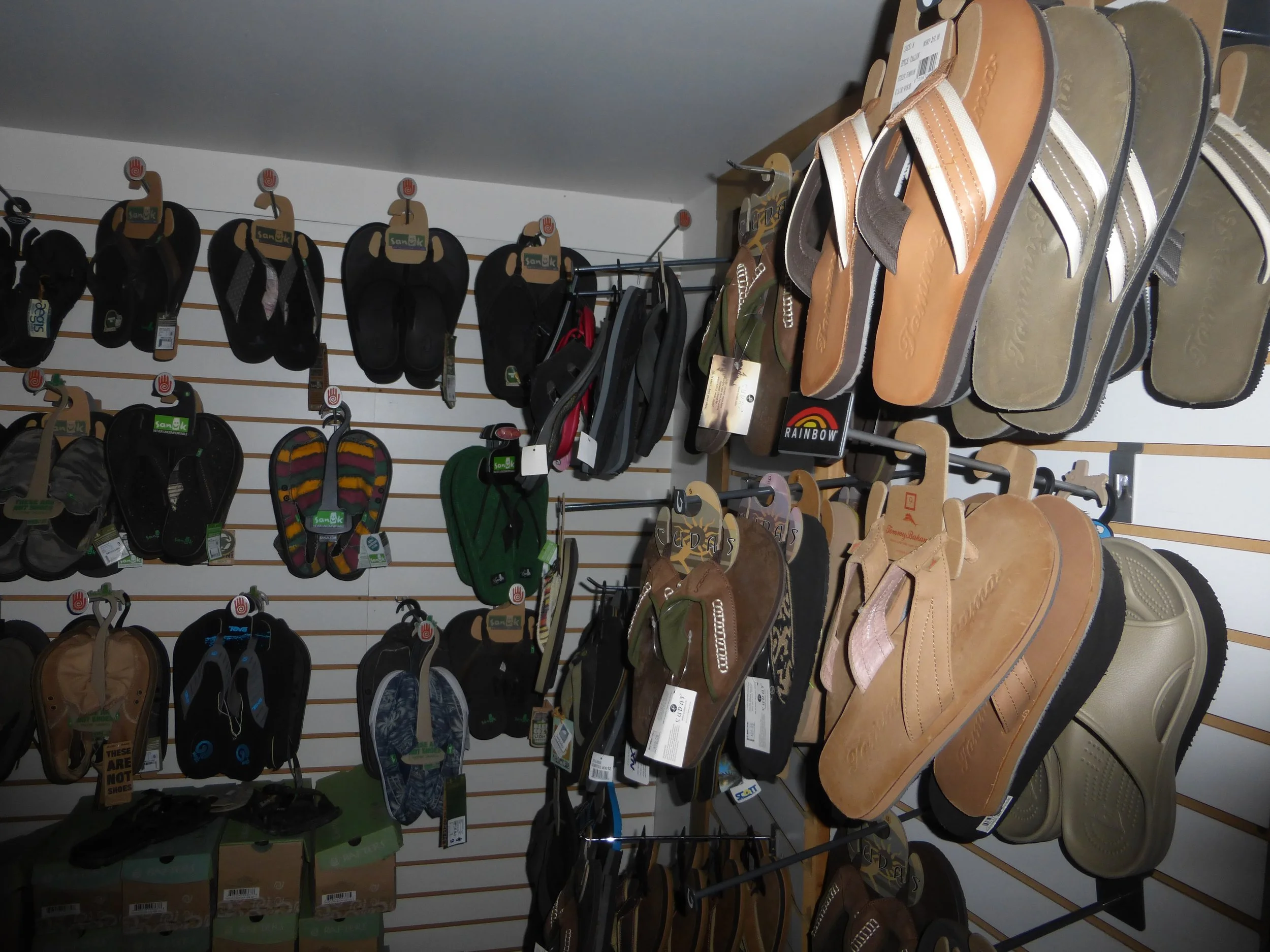 Wall display of various styles and colors of sandals and flip-flops in a store, organized on hooks.