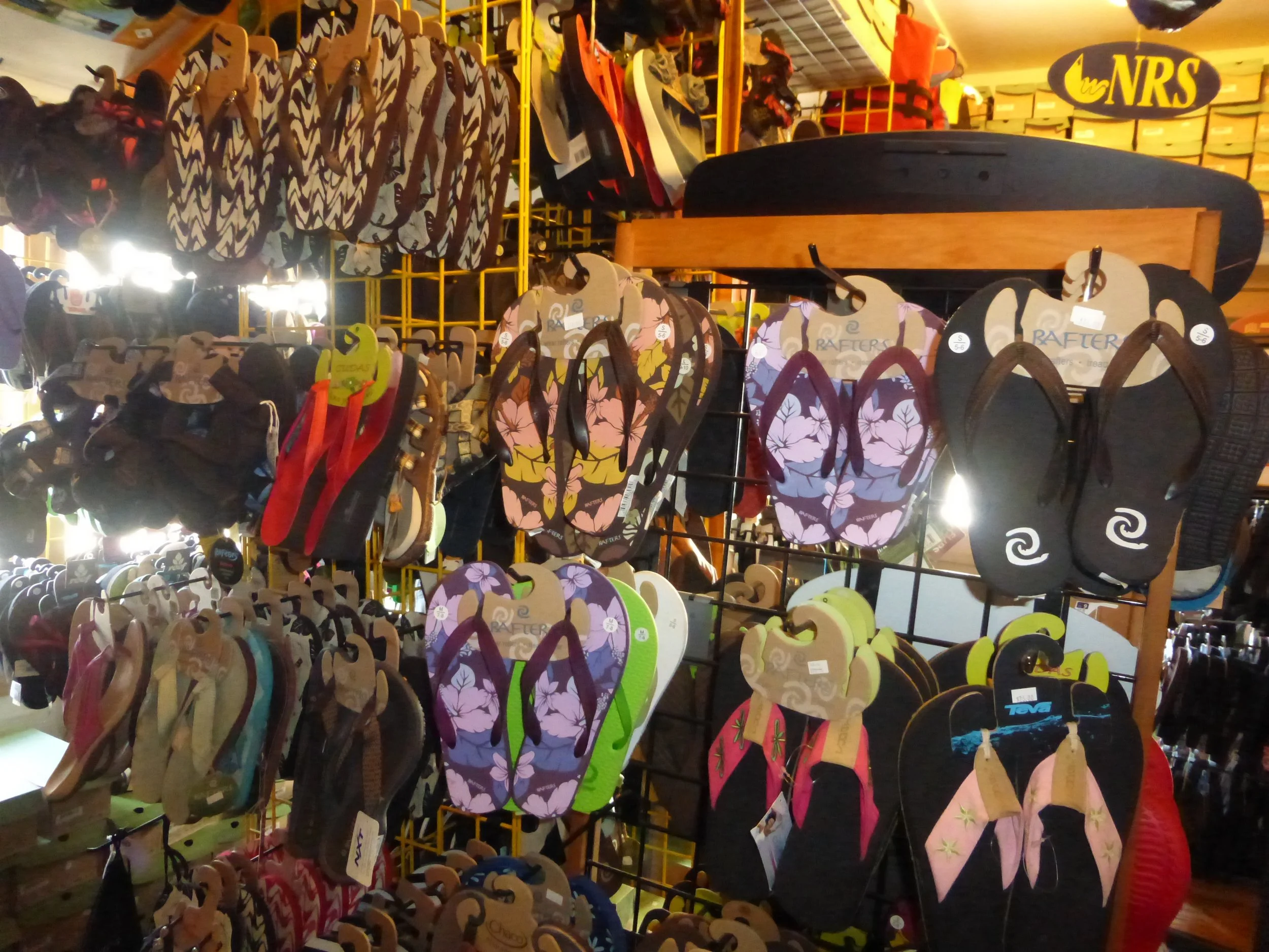 Various flip flops on display at a store, showcasing different colors and patterns, including floral and geometric designs, hanging on a metal rack.