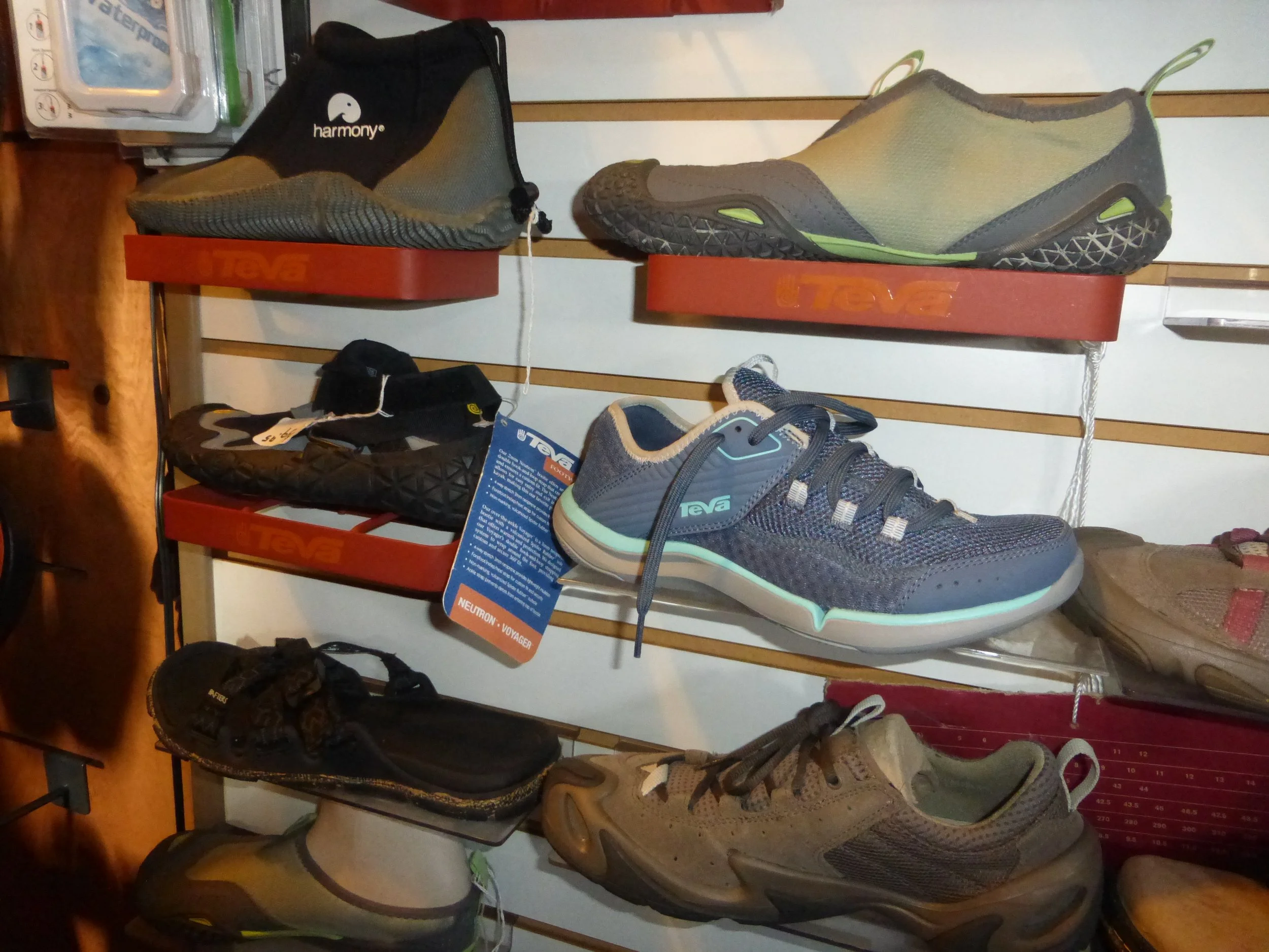 Rack displaying various Teva, Chaco, Rainbow, Harmony, Reef brand shoes including water shoes, sandals, and athletic footwear in a store setting.