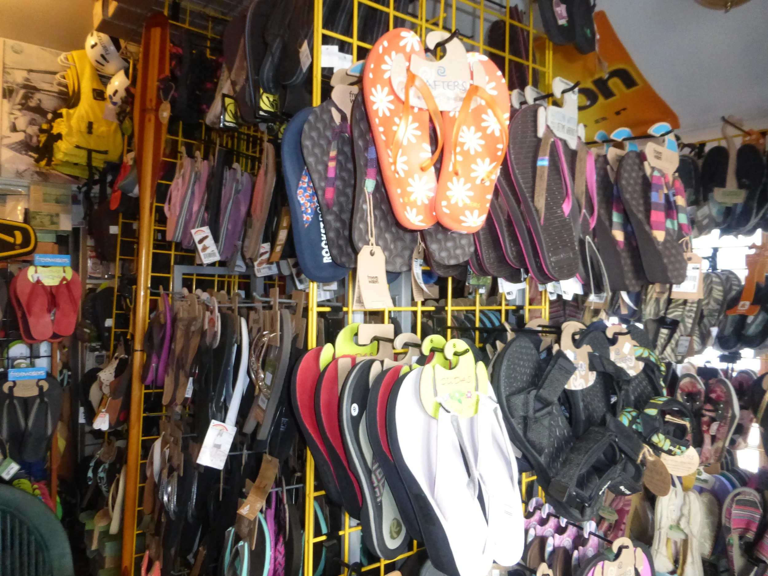 A shop display with various flip-flops and sandals hanging on yellow metal racks.