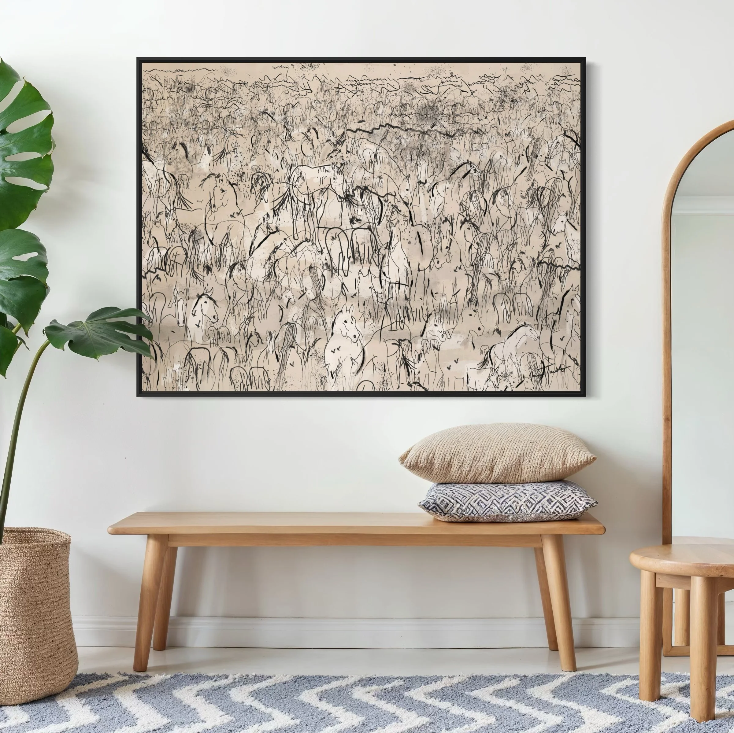 An interior wall with a large black-framed abstract line drawing of a herd of horses, a wooden bench with two pillows, a leafy plant in a woven basket, a wooden chair with a mirror nearby, and a striped rug on the floor.